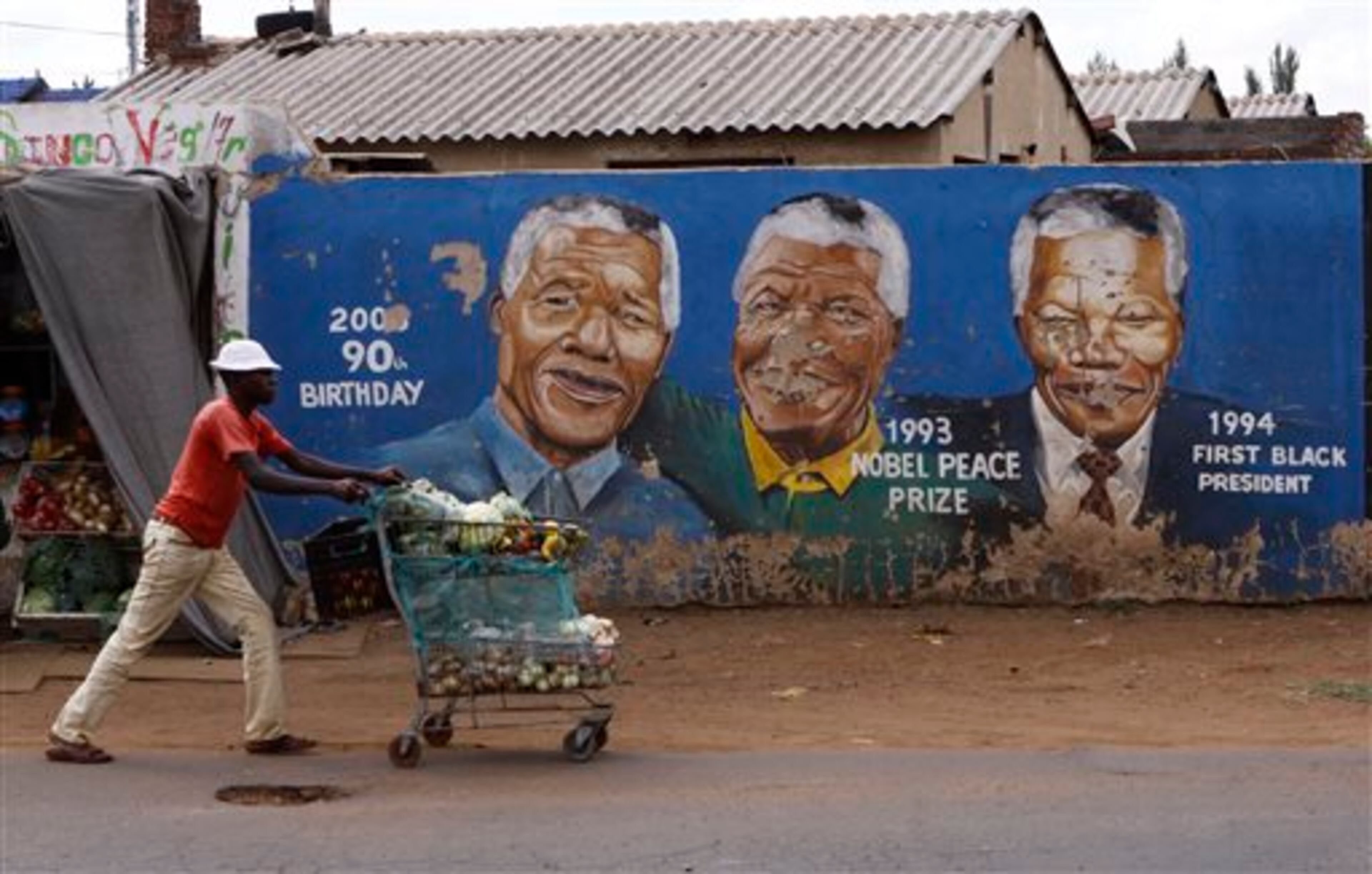 FILE - A hawker pushes his goods past portraits of former President Nelson Mandela depicted in various stages of his life along a street in Soweto, South Africa, in this March 28, 2013 file photo. The Nobel laureate is a revered figure in South Africa, which has honored his legacy of reconciliation by naming buildings and other places after him and printing his image on national banknotes. On Thursday, Dec. 5, 2013, Mandela died at the age of 95. (AP Photo/Denis Farrell, File)