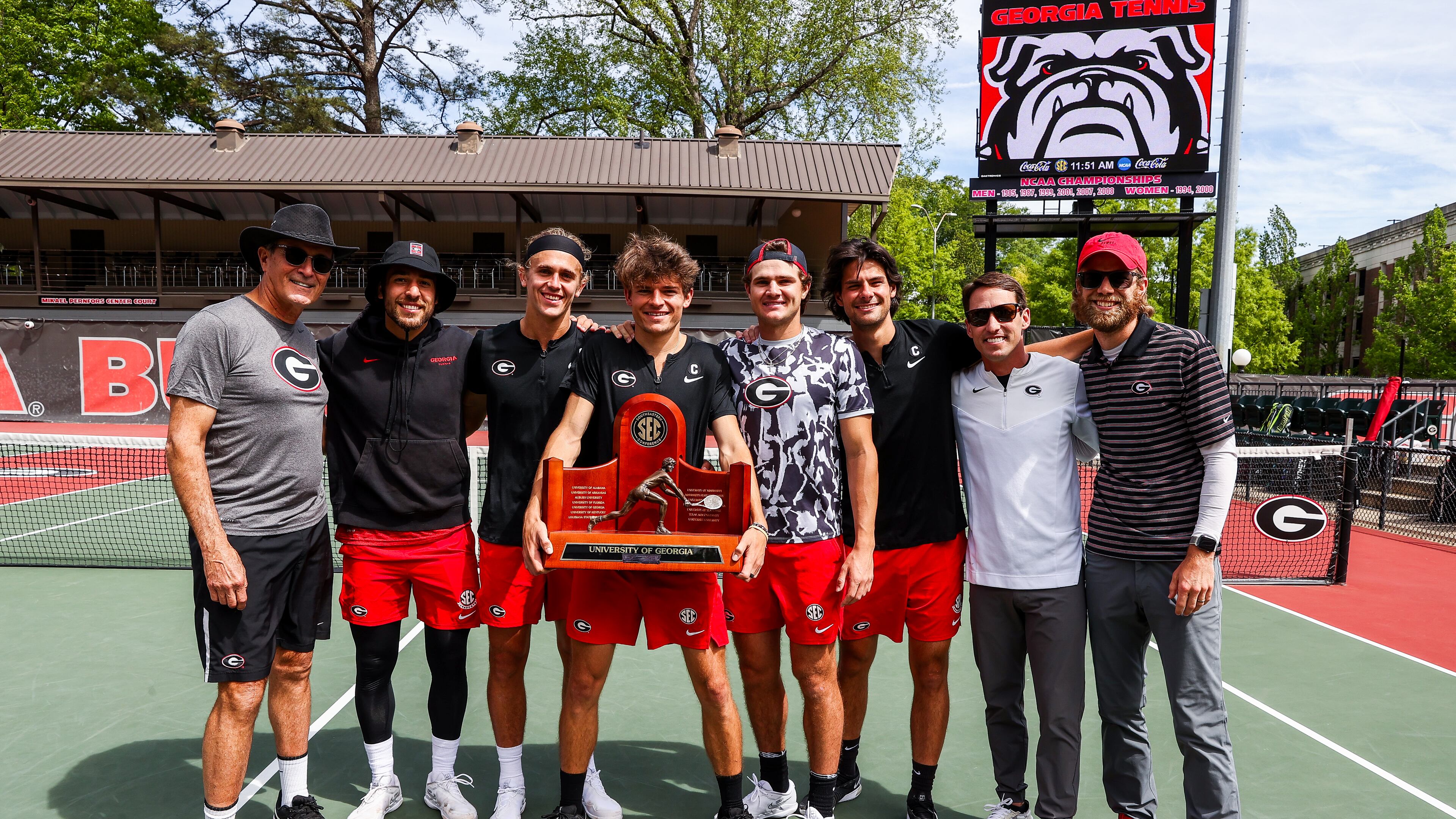 Georgia head coach Manuel Diaz (L) and players Teodor Giusca, Philip Henning, Britton Johnston, Trent Bryde, Blake Croyder, associate head coach Jamie Hunt, Georgia volunteer assistant coach Will Reynolds pose with the SEC championship trophy after clinching the regular-season title against Mississippi State on Thursday at Dan Magill Tennis Complex in Athens. (Tony Walsh/UGA Athletics)