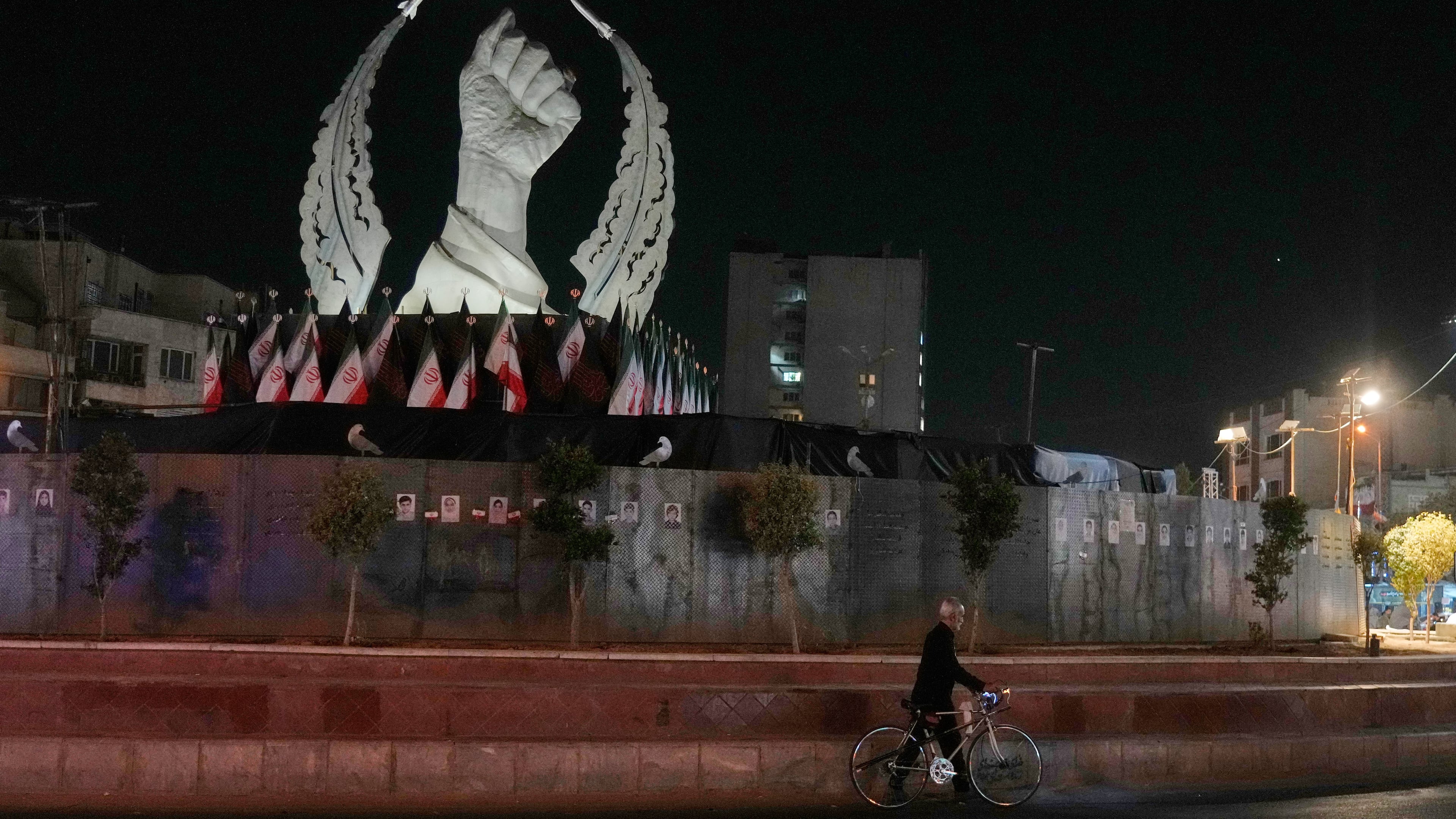 A man carries his bicycle in front of a monument depicting the clenched fist of the late Iranian Supreme Leader Ayatollah Ali Khamenei, who was killed in the U.S. and Israel strike on Feb. 28, in Islamic Revolution Square in Tehran, Sunday, July 19, 2026. (AP Photo/Vahid Salemi)