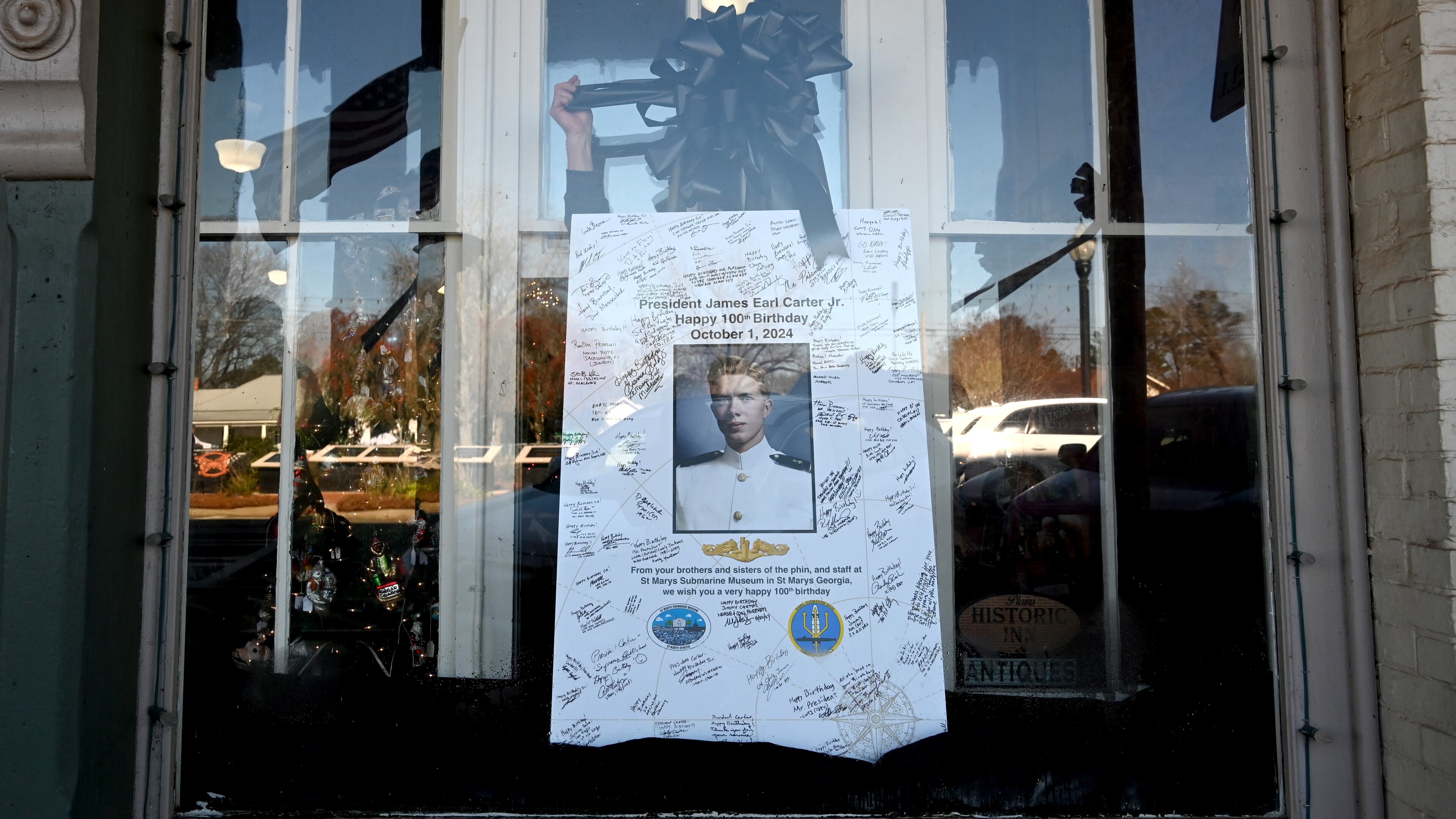 Tim Buchanan (hand), manager of the Buffalo Cafe, decorates a portrait of former President Jimmy Carter with a black ribbon, in downtown Plains, Wednesday, January 8, 2025. (Hyosub Shin / AJC)