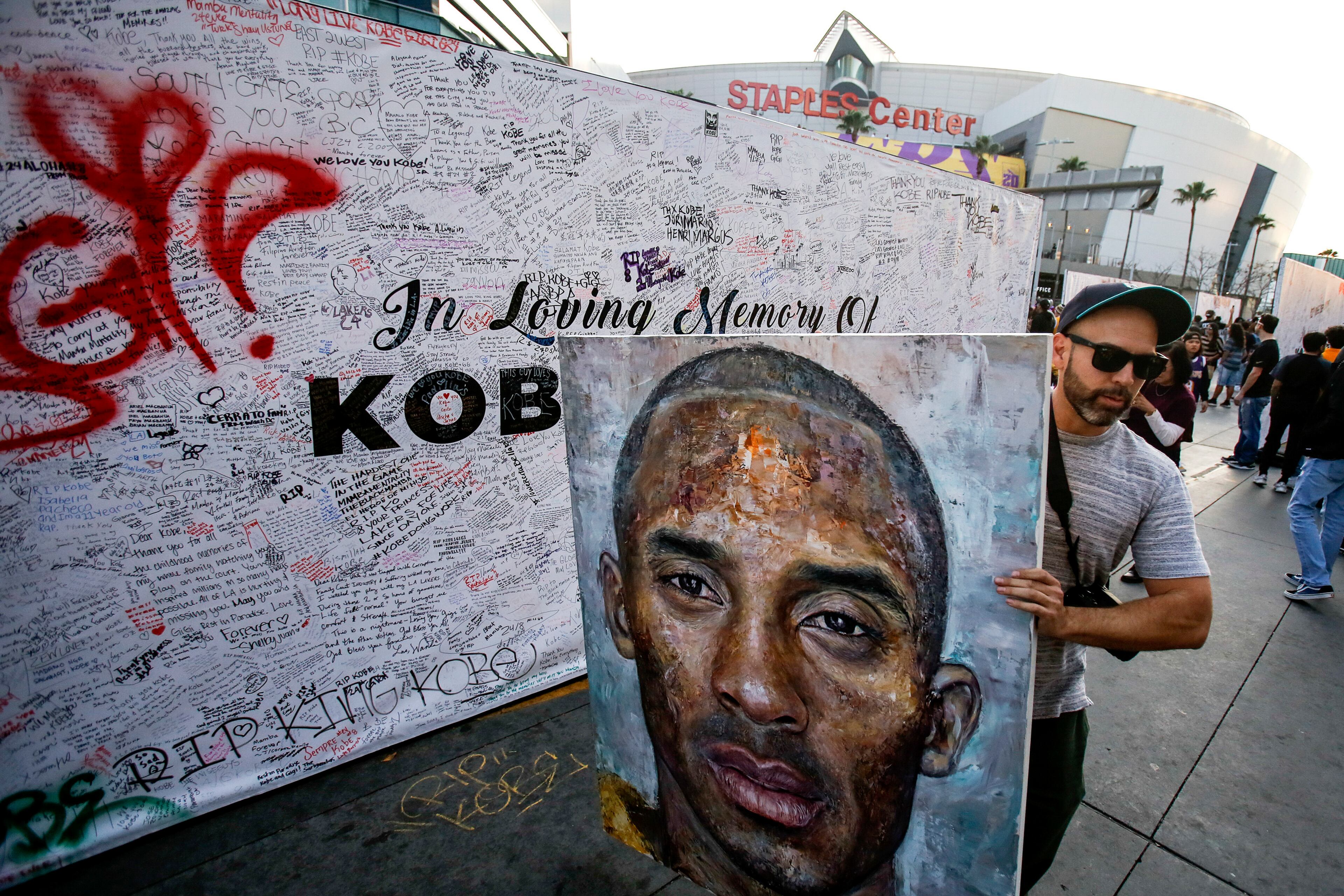 Paul Daniel shows a painting of the lake Kobe Bryant, at a memorial in front of Staples Center prior to an NBA game between the Los Angeles Lakers and the Portland Trail Blazers, Friday, Jan. 31, 2020, in Los Angeles. Bryant, the 18-time NBA All-Star who won five championships and became one of the greatest basketball players of his generation during a 20-year career with the Lakers, died in a helicopter crash Sunday. (AP Photo/Ringo H.W. Chiu)