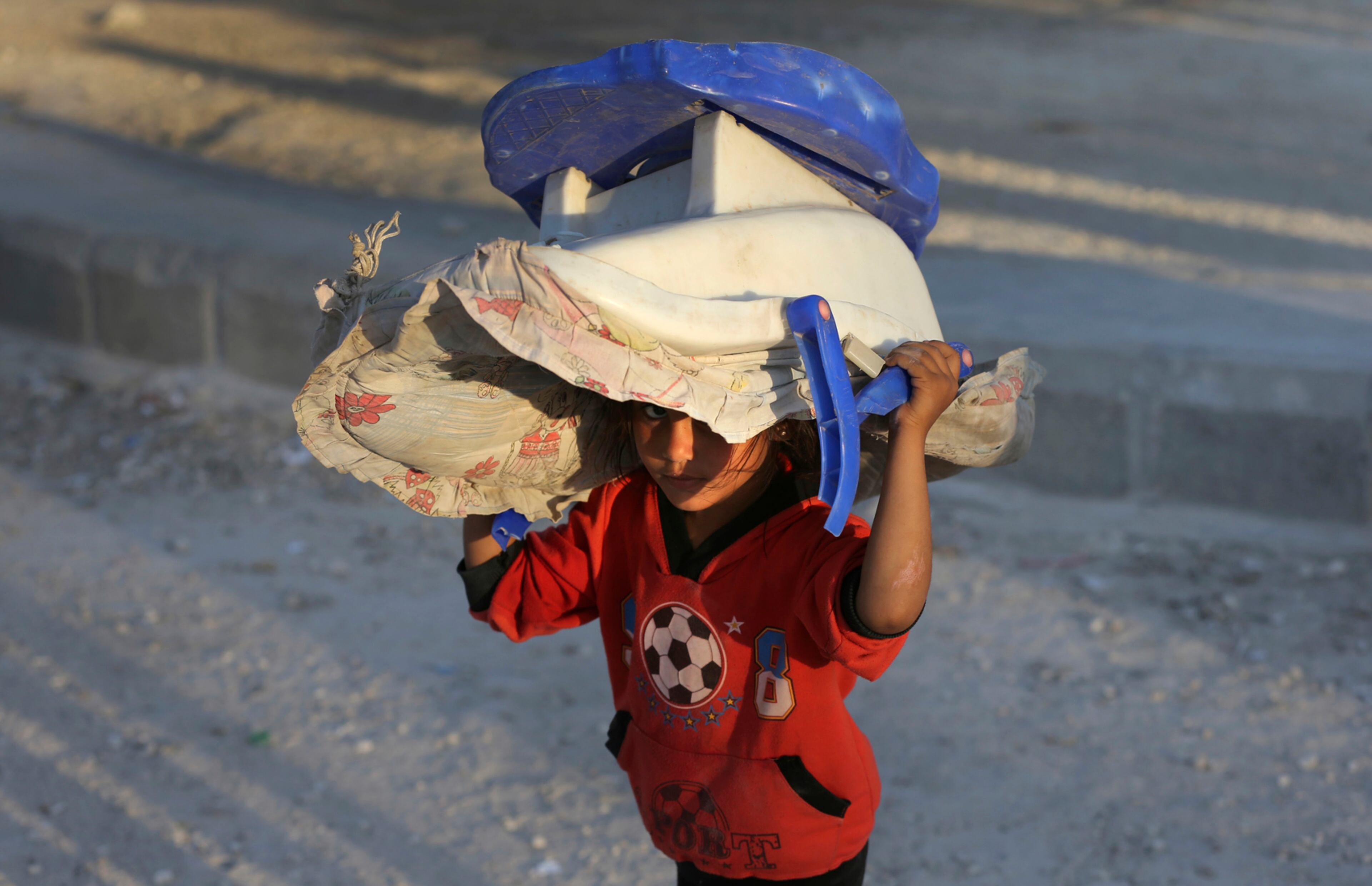A Syrian displaced young girl who fled with her family the battle between U.S.-backed Syrian Democratic Forces (SDF) and the Islamic State militants from Raqqa city, carries a baby carseat on her head upon her arrival at a refugee camp, in Ain Issa town, northeast Syria, Monday, July 24, 2017. The U.S. military is supporting local Syrian forces in a campaign to drive IS from Raqqa. (AP Photo/Hussein Malla)