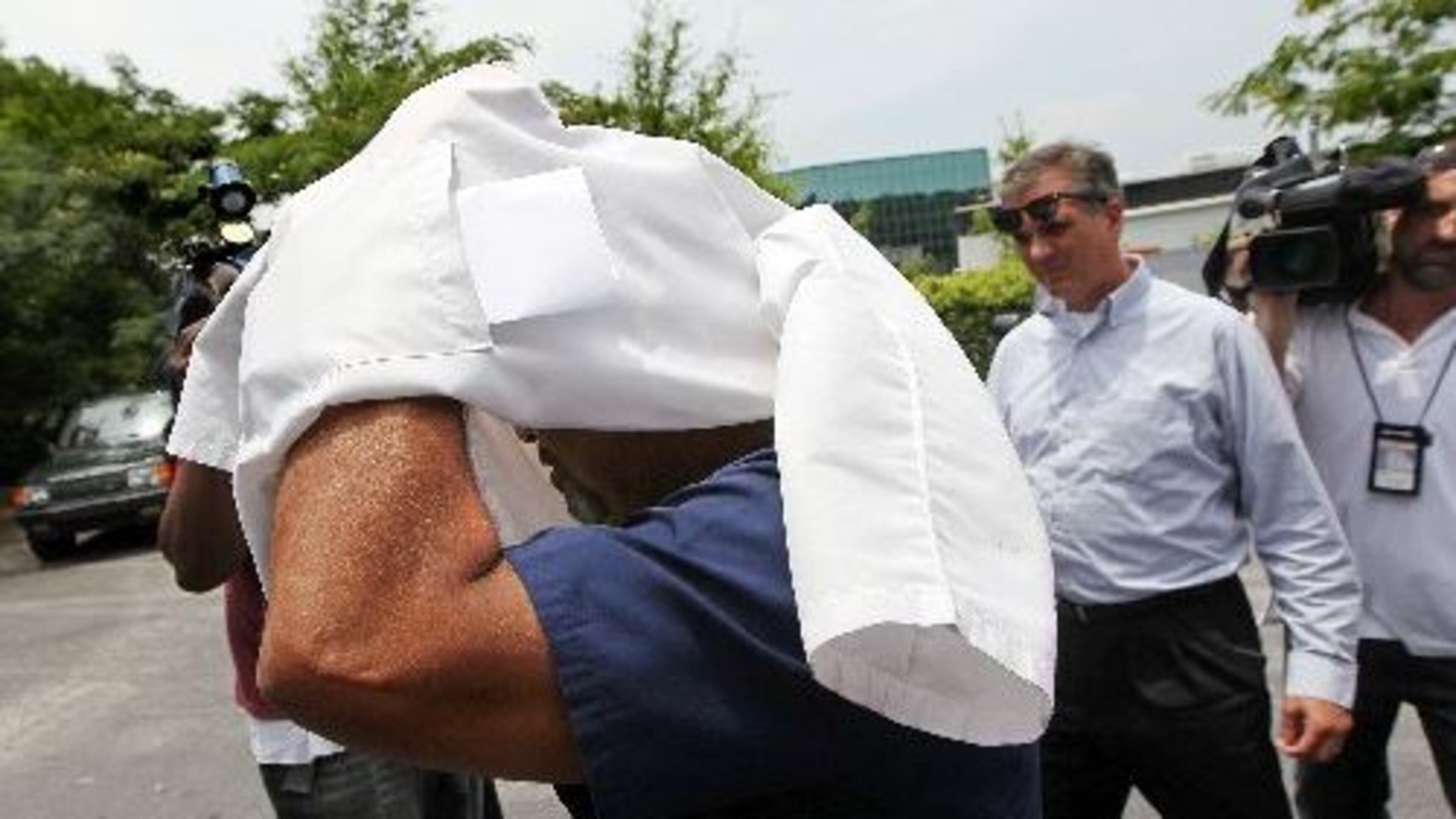 A doctor covers his head as he leaves during a ” pill mill” raid near Tucker in 2012. More than a half dozen patients were taken away in cuffs to a prisoner transport van. The doctors and employees were allowed to leave following the raid. The owner of the business was also removed in cuffs and taken away in a prisoner transport van. CURTIS COMPTON / CCOMPTON@AJC.COM AJC File Photo