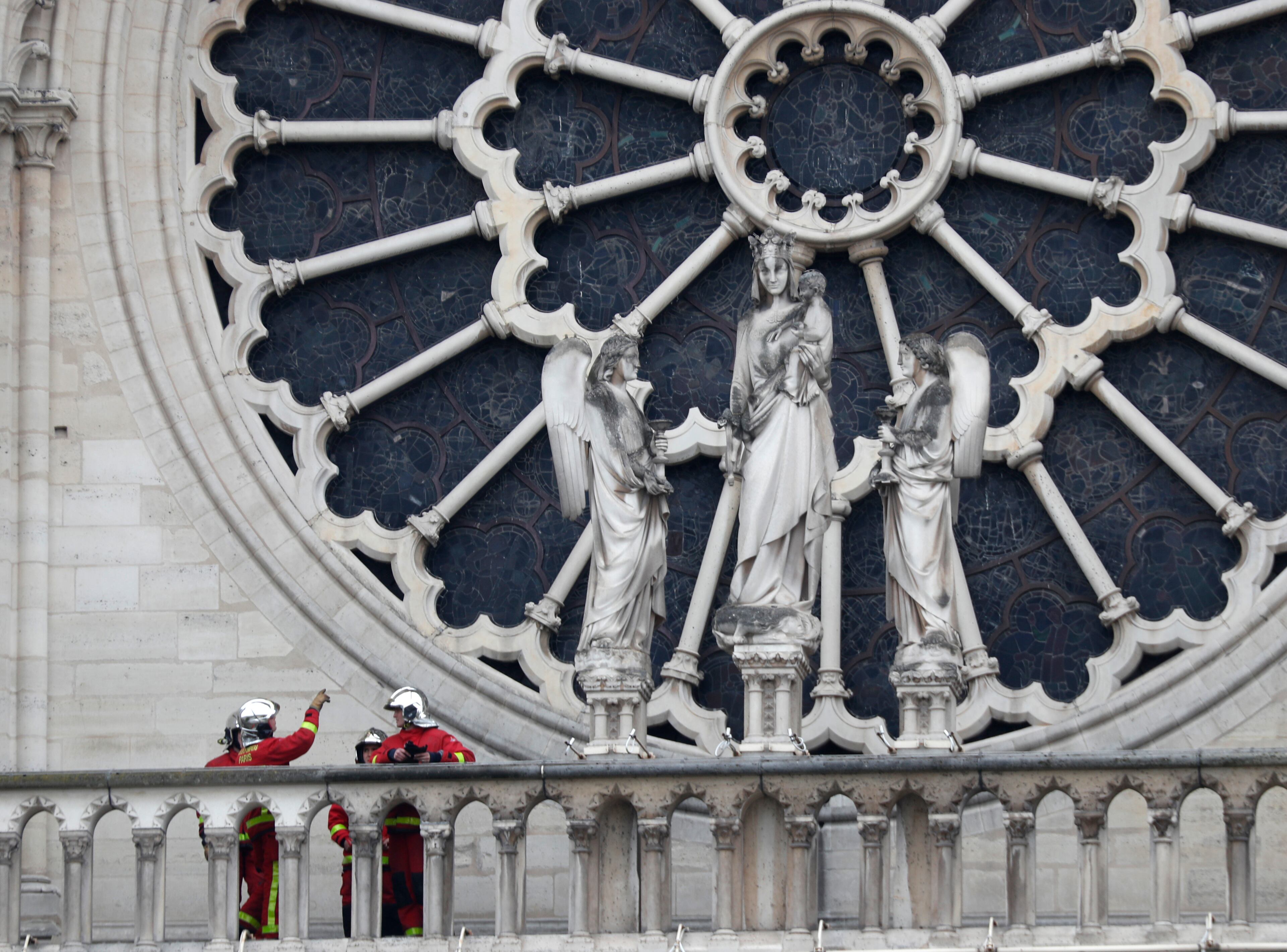 Firefighters talk near the rose window of Notre Dame cathedral Tuesday April 16, 2019 in Paris. Experts assessed the blackened shell of Paris' iconic Notre Dame Tuesday morning to establish next steps to save what remains after a devastating fire destroyed much of the cathedral that had survived almost 900 years of history. (AP Photo/Thibault Camus)