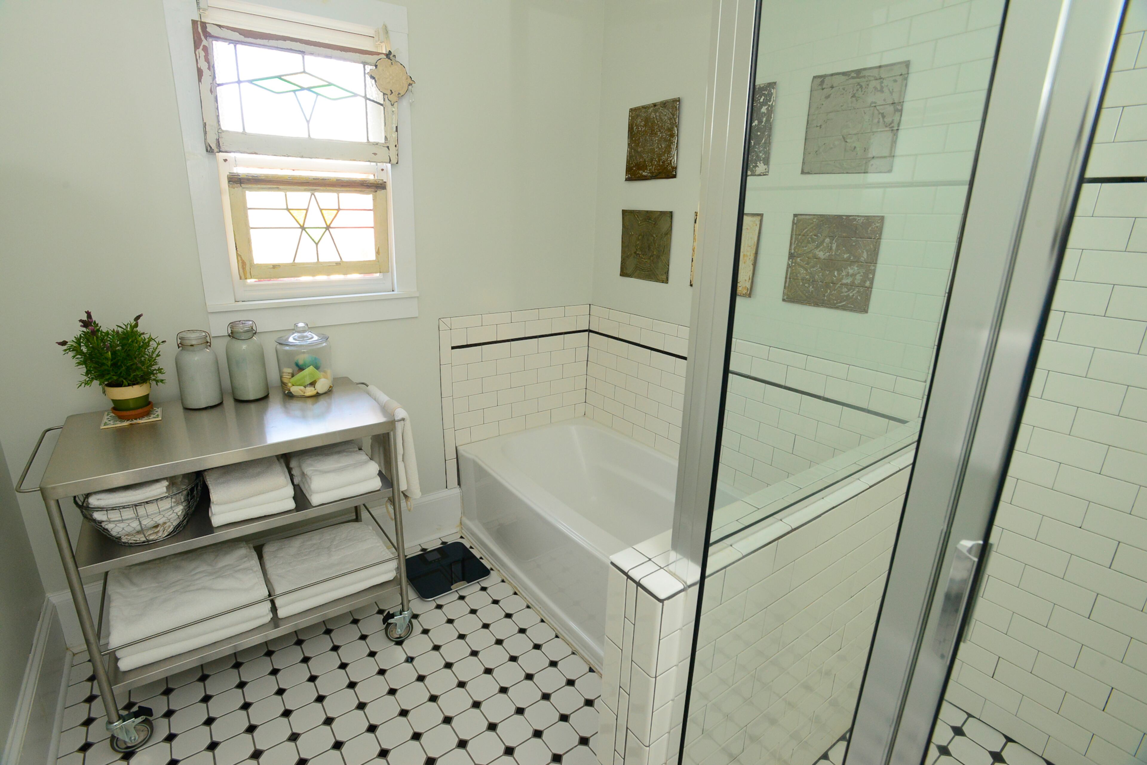 A stainless steel cart provides a creative way to store towels in the master bathroom, which features subway tile, antique windows and tin art elements.