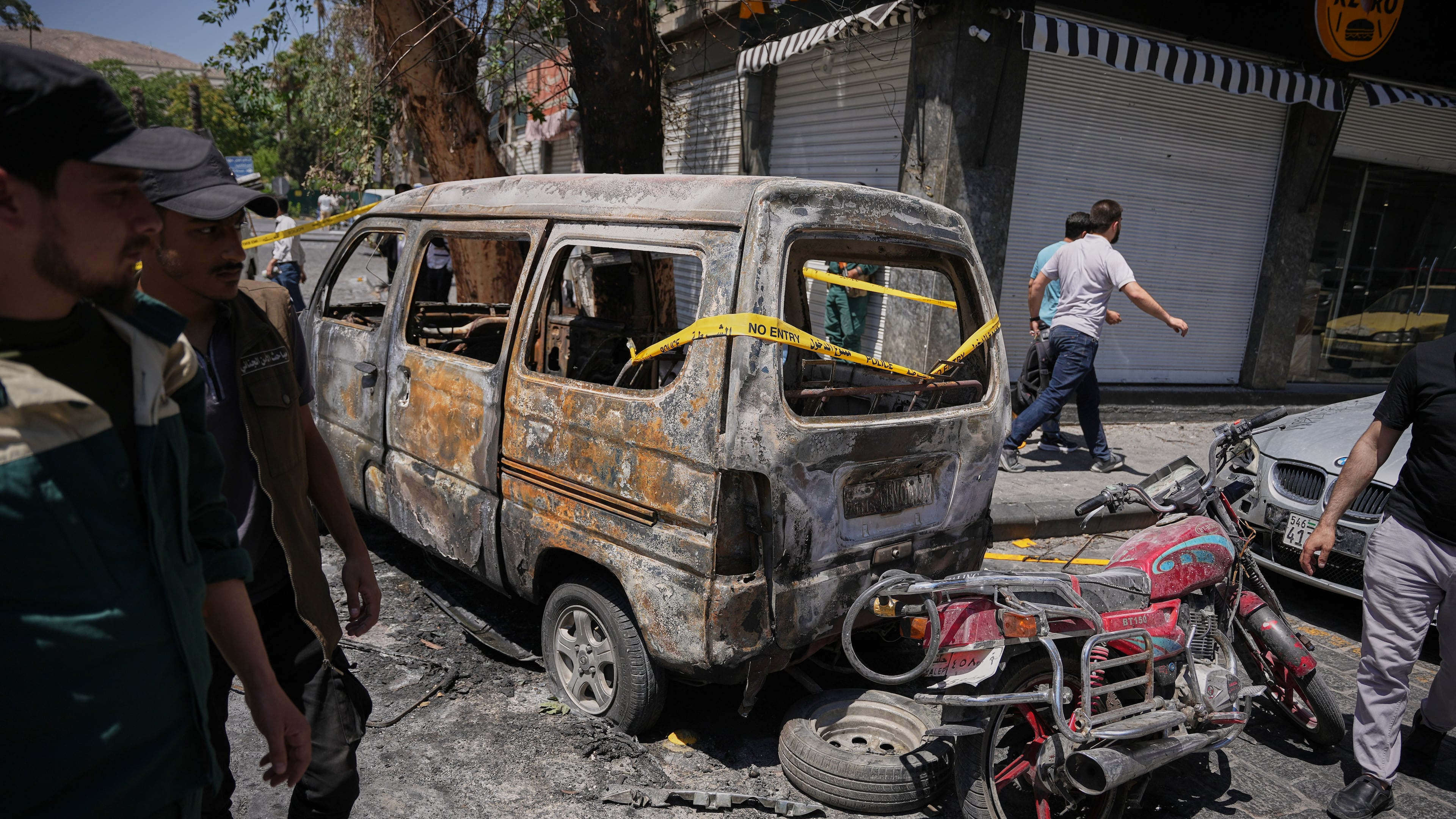 Syrian security personnel inspect a burned vehicles near the Four Seasons Hotel after two explosions rocked the area earlier while Syrian President Ahmad al-Sharaa was meeting French President Emmanuel Macron at the presidential palace, in Damascus, Syria, Tuesday, July 7, 2026. (AP Photo/Omar Albam)