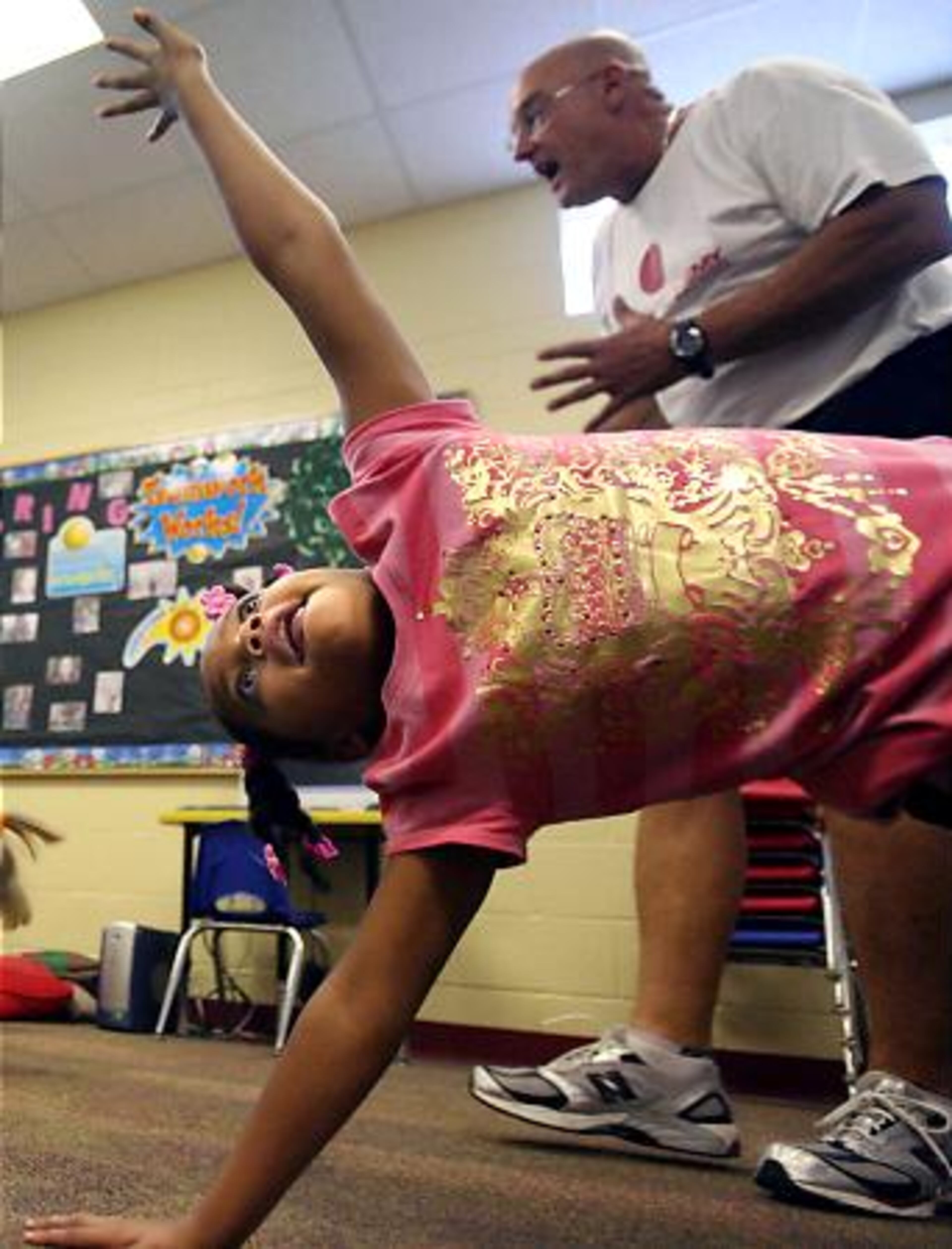 Maya Richards, 6, balances on one hand and one leg as coach Jim Cooper instructs other kindergarten and first grade students.