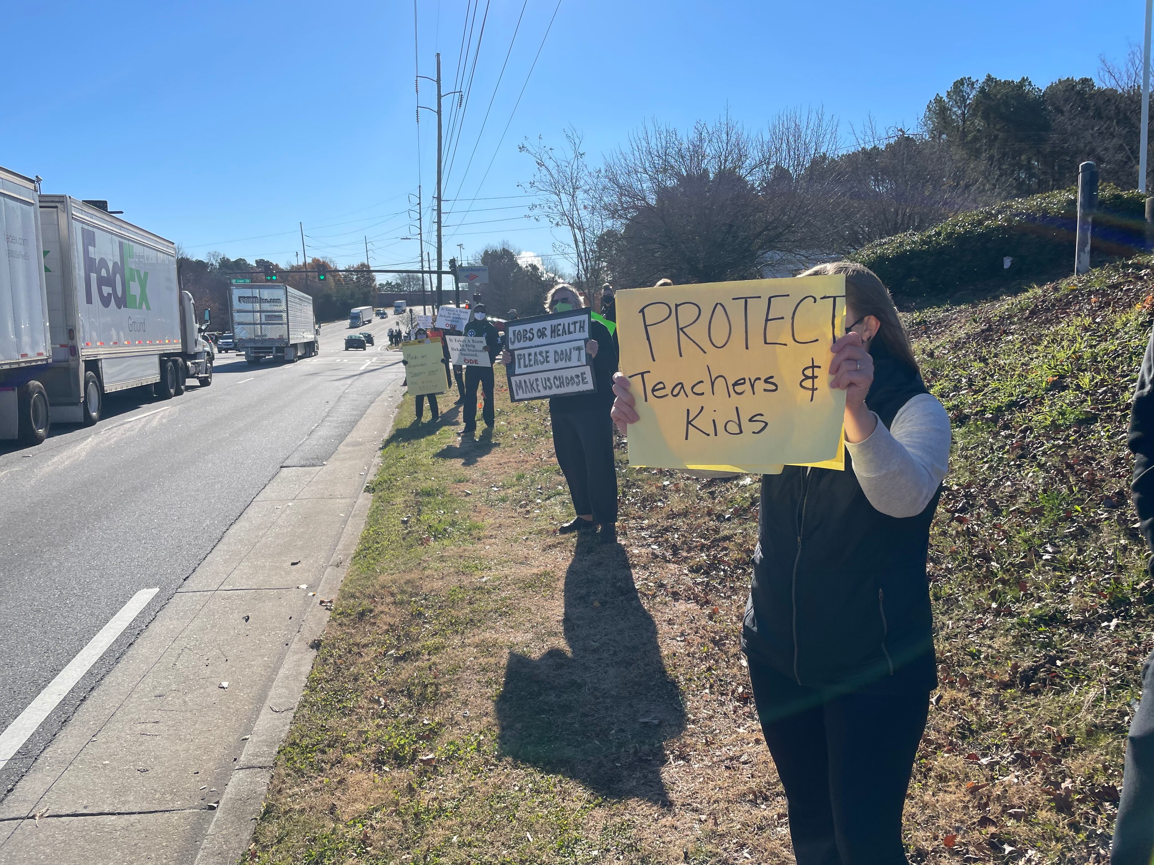 Community members in DeKalb held signs on Tuesday to protest against the reopening of DeKalb County schools.