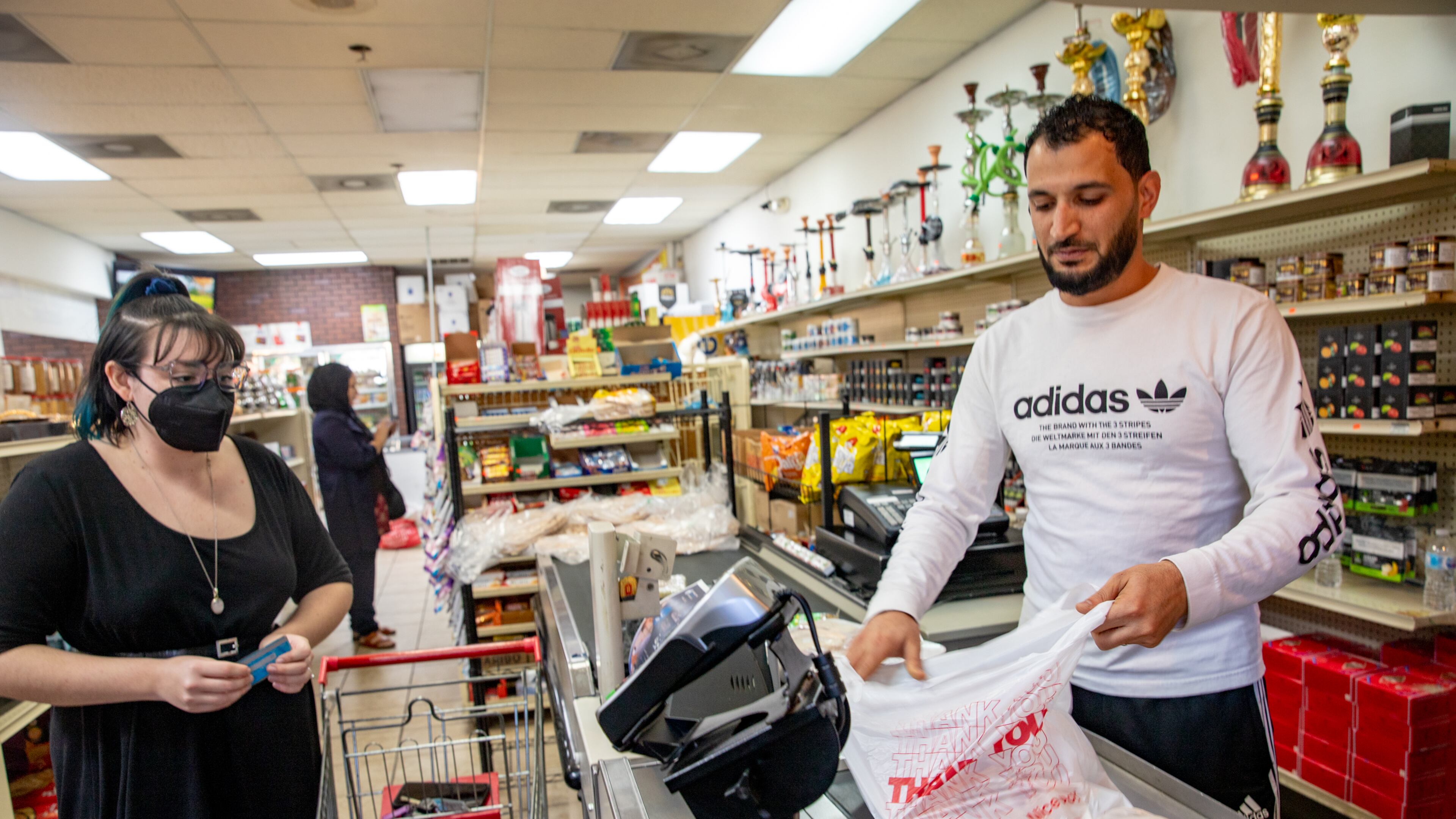 New American Pathway staff China Myrick, left, check out with Raghb Moshaal, right, at Al-Salam International Groceries in Clarkston Monday, November 22, 2021 as they prepare for an Afghan family of five, with one on the way, to arrive and relocate to the community. The family of two adults and three small children will need to make the food last two weeks and the organization is also preparing an apartment for the refugee family. (Jenni Girtman for The Atlanta Journal-Constitution)