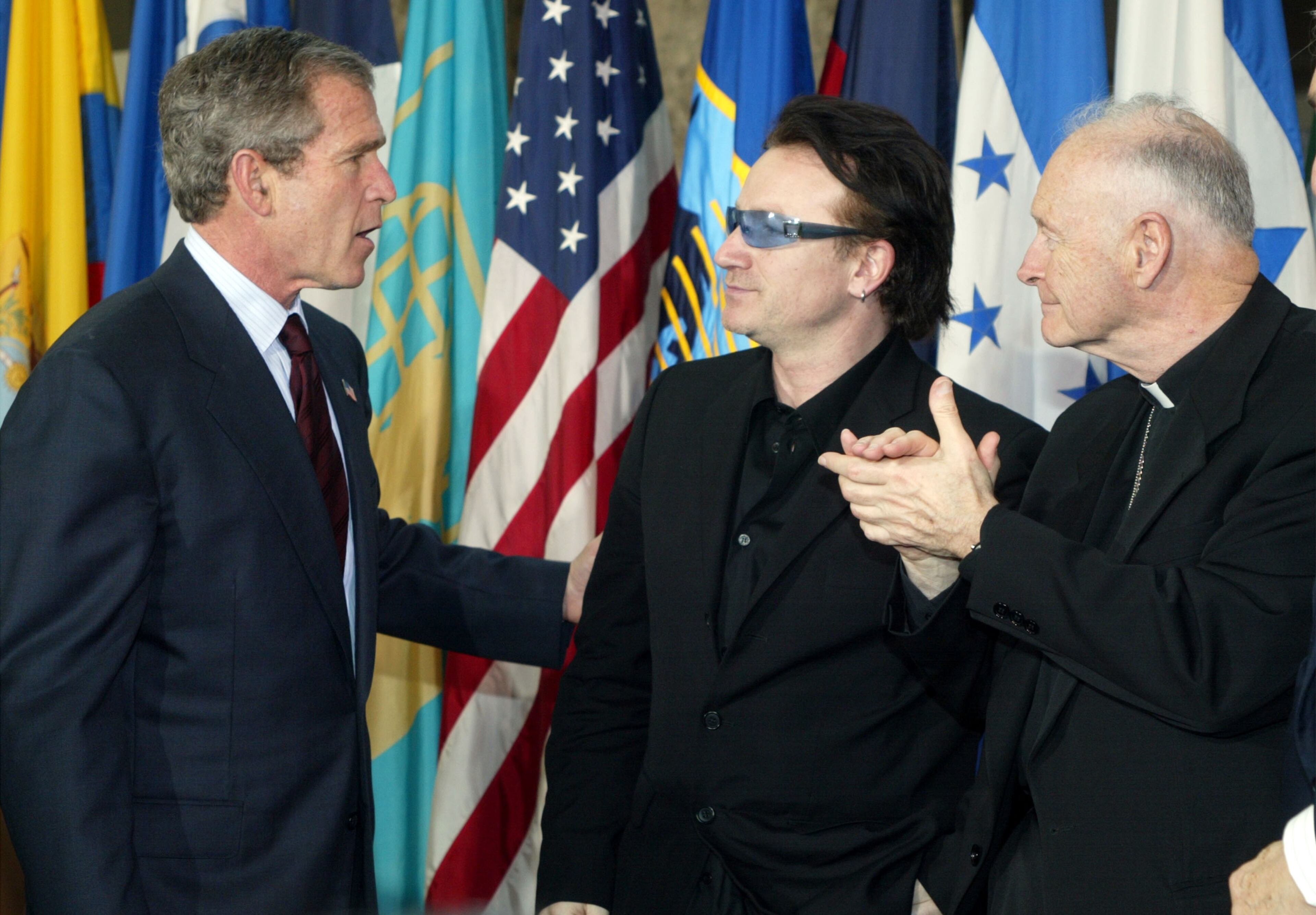 (L-R): U.S. President George W. Bush speaks with Bono, the lead singer of Irish pop group U2, as Archbishop of Washington, Cardinal Theodore E. McCarrick, looks on March 14, 2002 during an Inter-American Development Bank event in Washington, DC. President Bush announced that he would offer an extra $5 billion in aid to poor nations that embrace economic and political reforms. (Photo by Alex Wong/Getty Images)