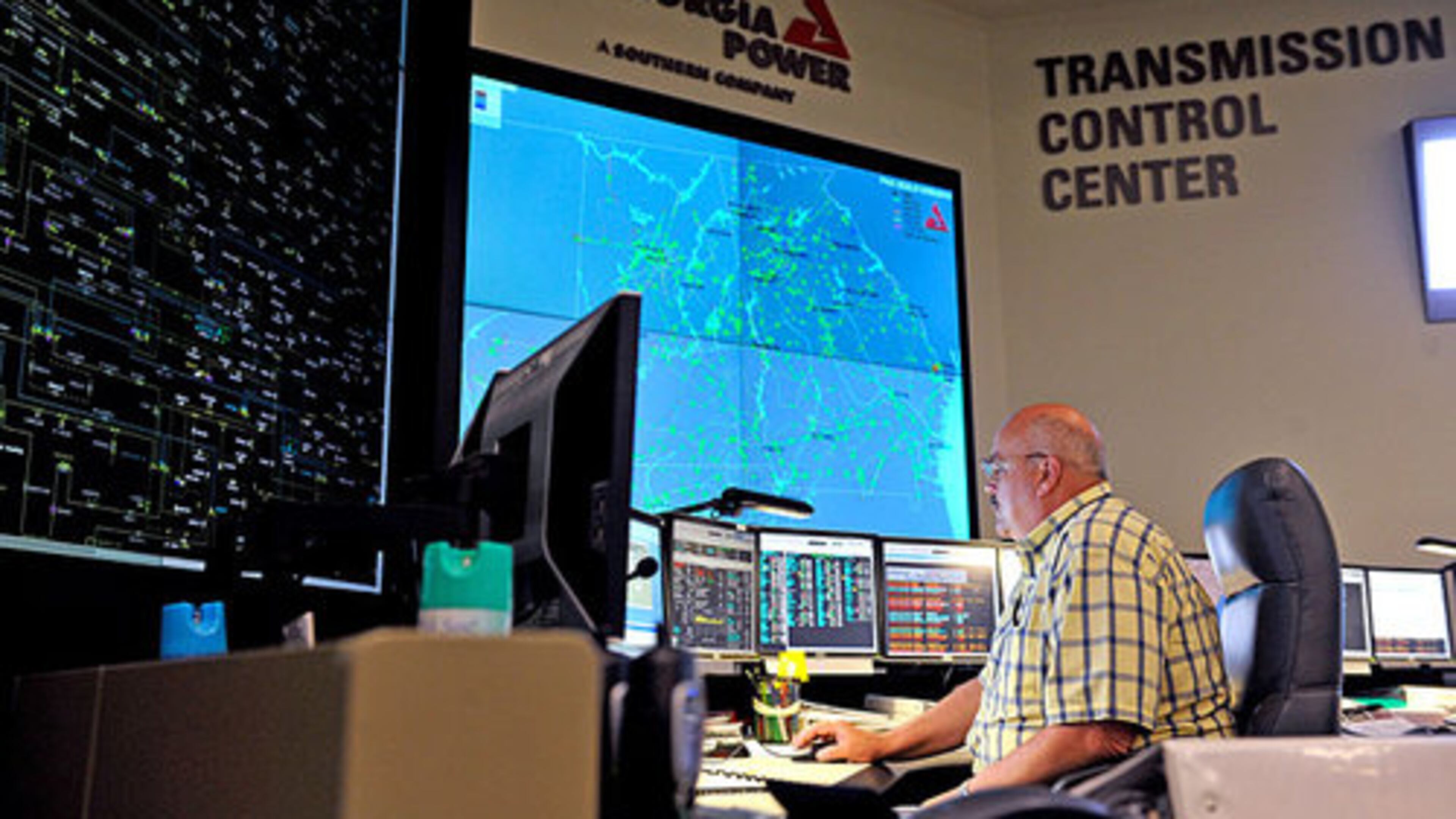 Gerald Snodgrass sits in front of the large electronic mimic board (left), which displays the status of transmission lines and substations around the state, and a smaller screen (right) which shows the Southern Company load flow from Mississippi to the Florida panhandle, at the Georgia Transmission Control Center at Georgia Power.