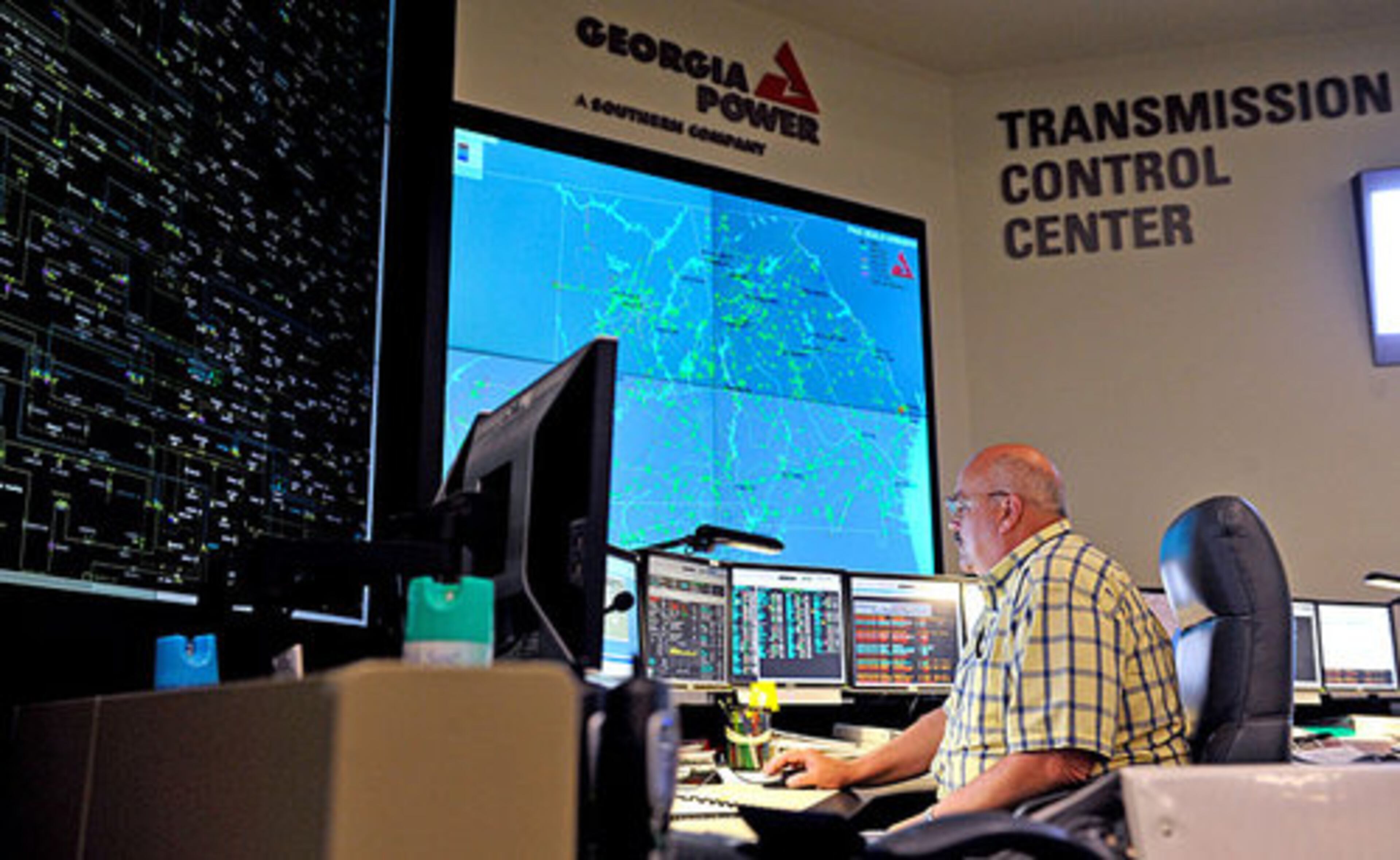 Gerald Snodgrass sits in front of the large electronic mimic board (left), which displays the status of transmission lines and substations around the state, and a smaller screen (right) which shows the Southern Company load flow from Mississippi to the Florida panhandle, at the Georgia Transmission Control Center at Georgia Power.
