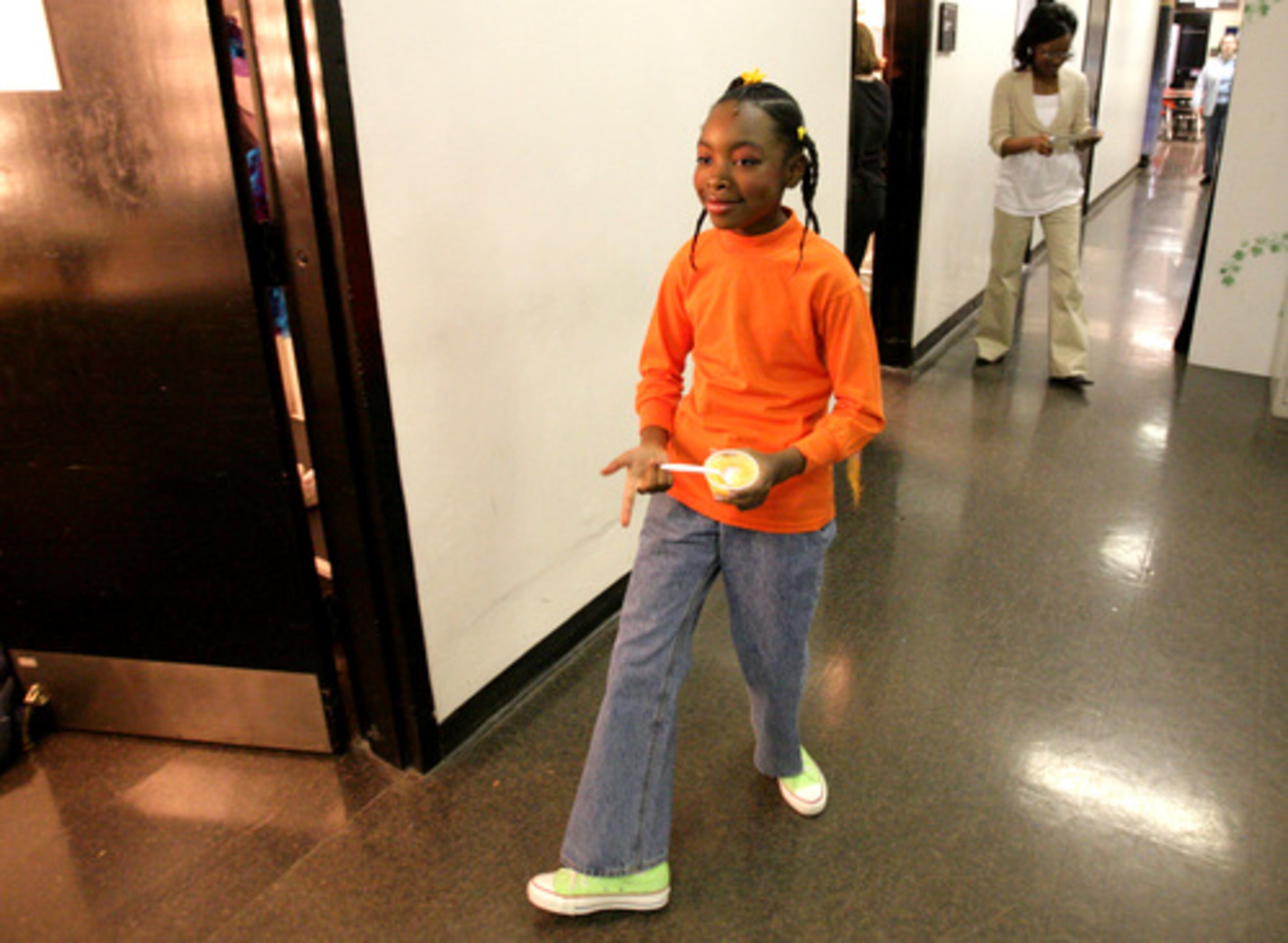Jamiah walks the hall between the dressing rooms with her breakfast, apple sauce.
