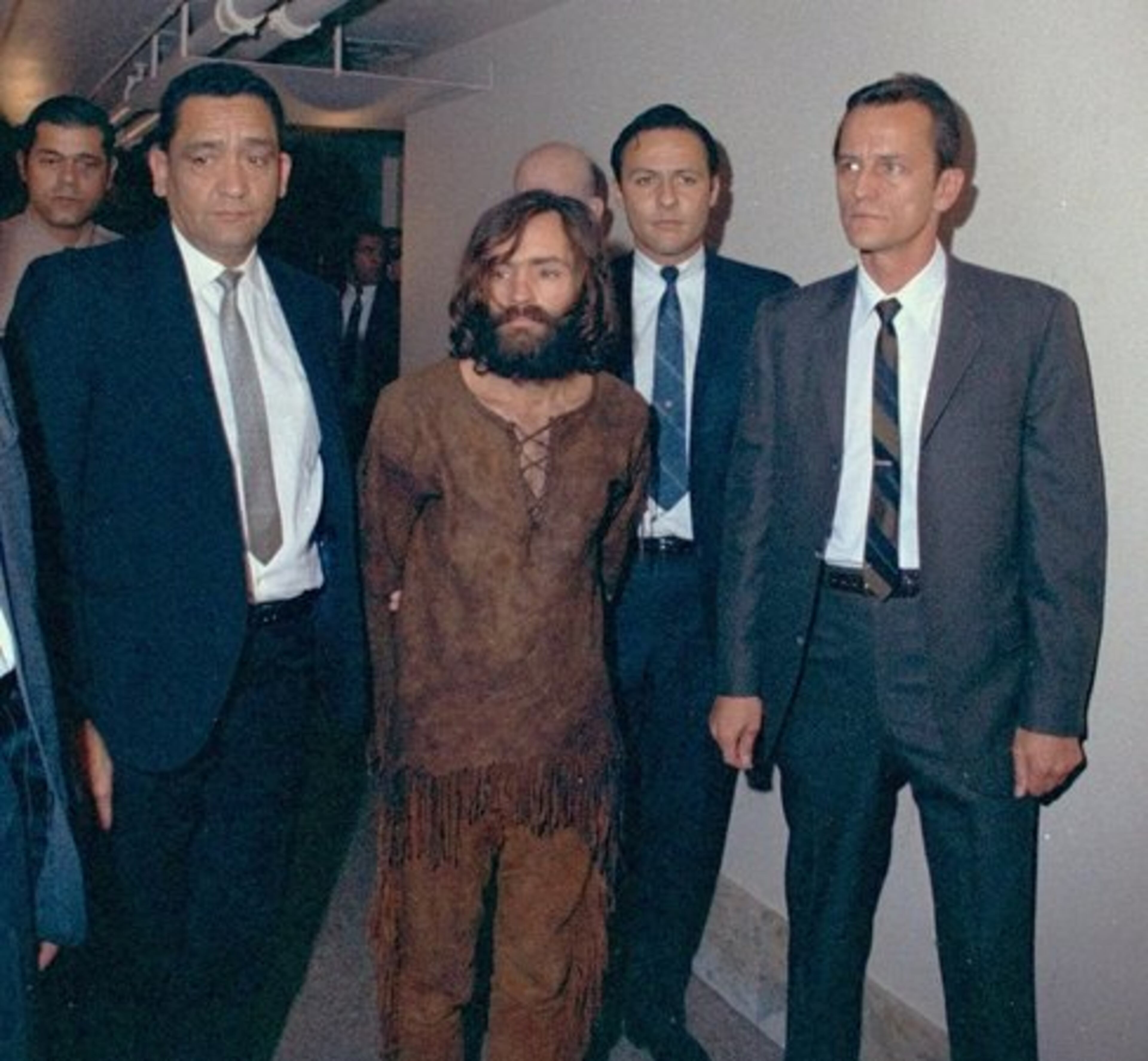 CHARLES MANSON (center), an aspiring singer with tenuous connections to Beach Boy Brian Wilson, and his followers commit a series of murders, including that of actress Sharon Tate.