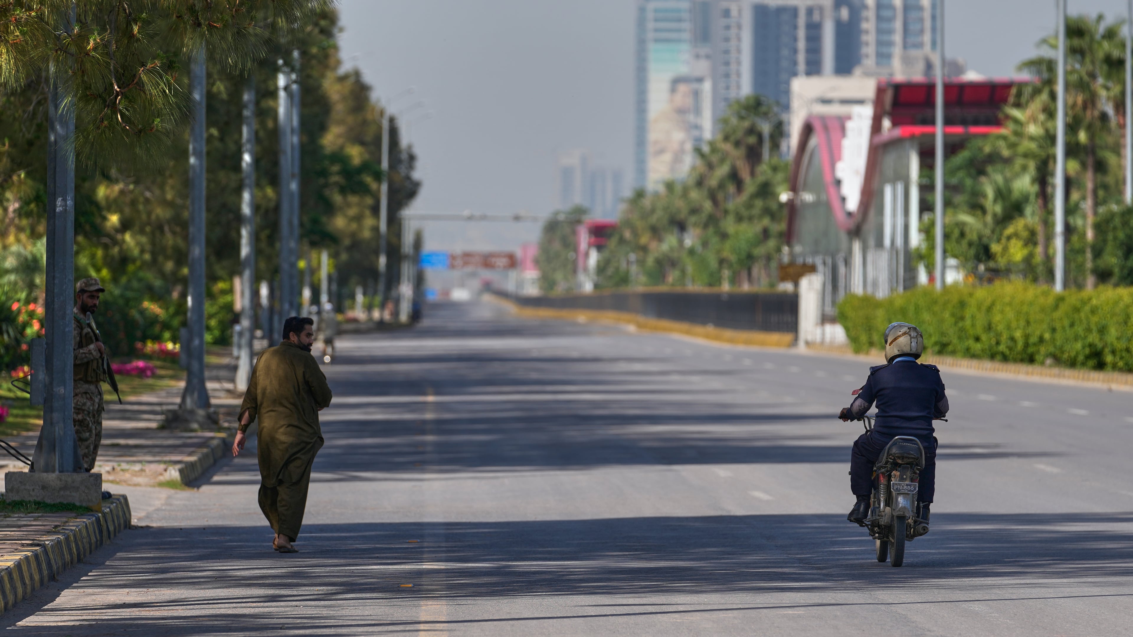An army soldier, left, walks as police officer drives motorcycle on an empty road ahead of second round of negotiations between the U.S. and Iran, in Islamabad, Pakistan, Monday, April 20, 2026. (AP Photo/Anjum Naveed)