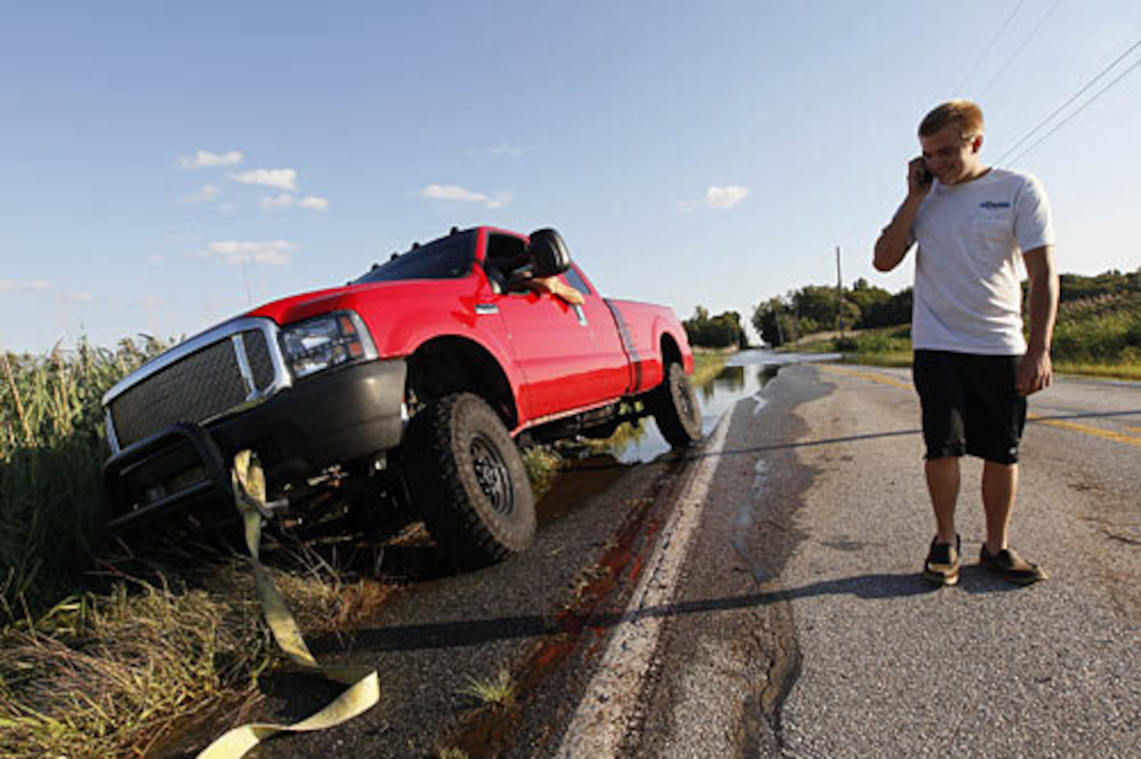 John Young makes a phone call as he waits to have his stuck pickup truck pulled out of a ditch on a partially flooded road in Port Penn, Del., Sunday, Aug. 28, 2011, after Hurricane Irene dropped several inches of rain along the Delaware coast overnight.
