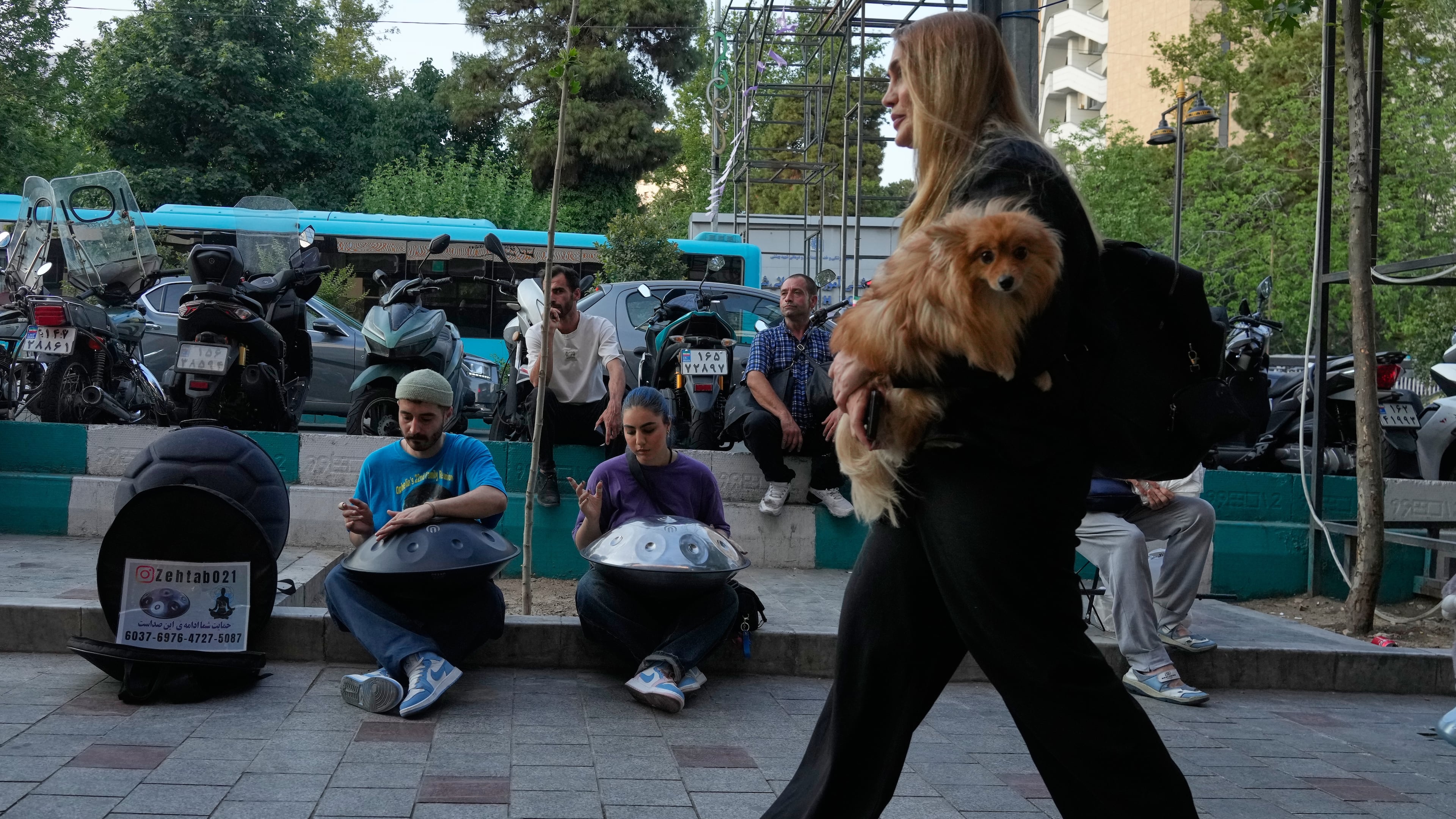 Street musicians play music as a woman carries a dog on a sidewalk in northern Tehran, Wednesday, June 10, 2026. (AP Photo/Vahid Salemi)