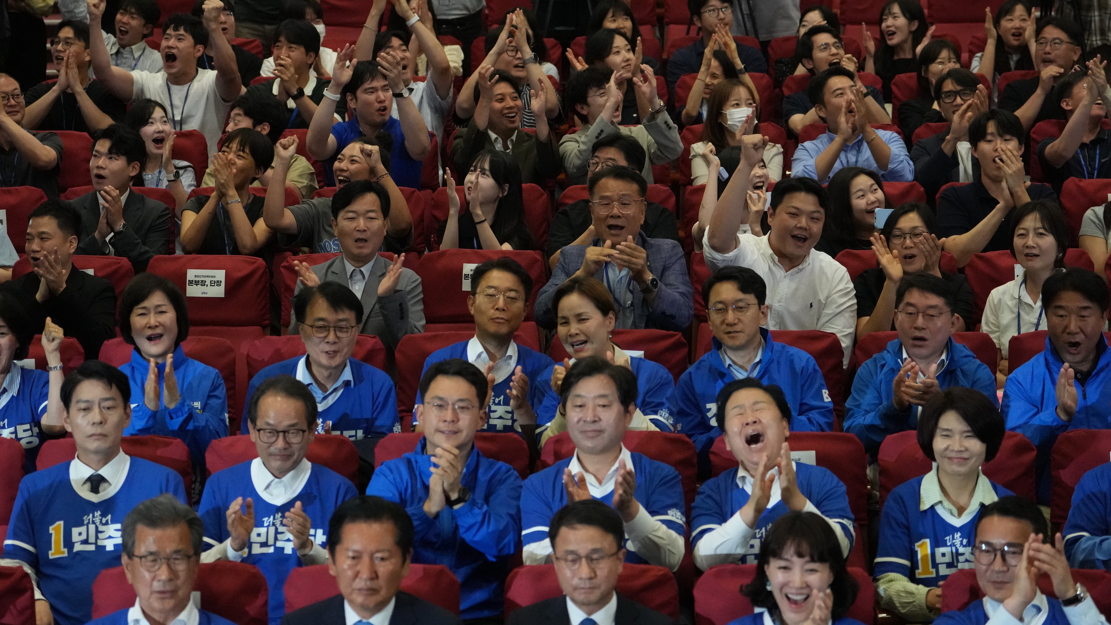 Lawmakers and members of South Korea's ruling Democratic Party react as they watch TV news program about results of exit polls for June 3 nationwide simultaneous local elections at the National Assembly in Seoul, South Korea, Wednesday, June 3, 2026. (AP Photo/Lee Jin-man)