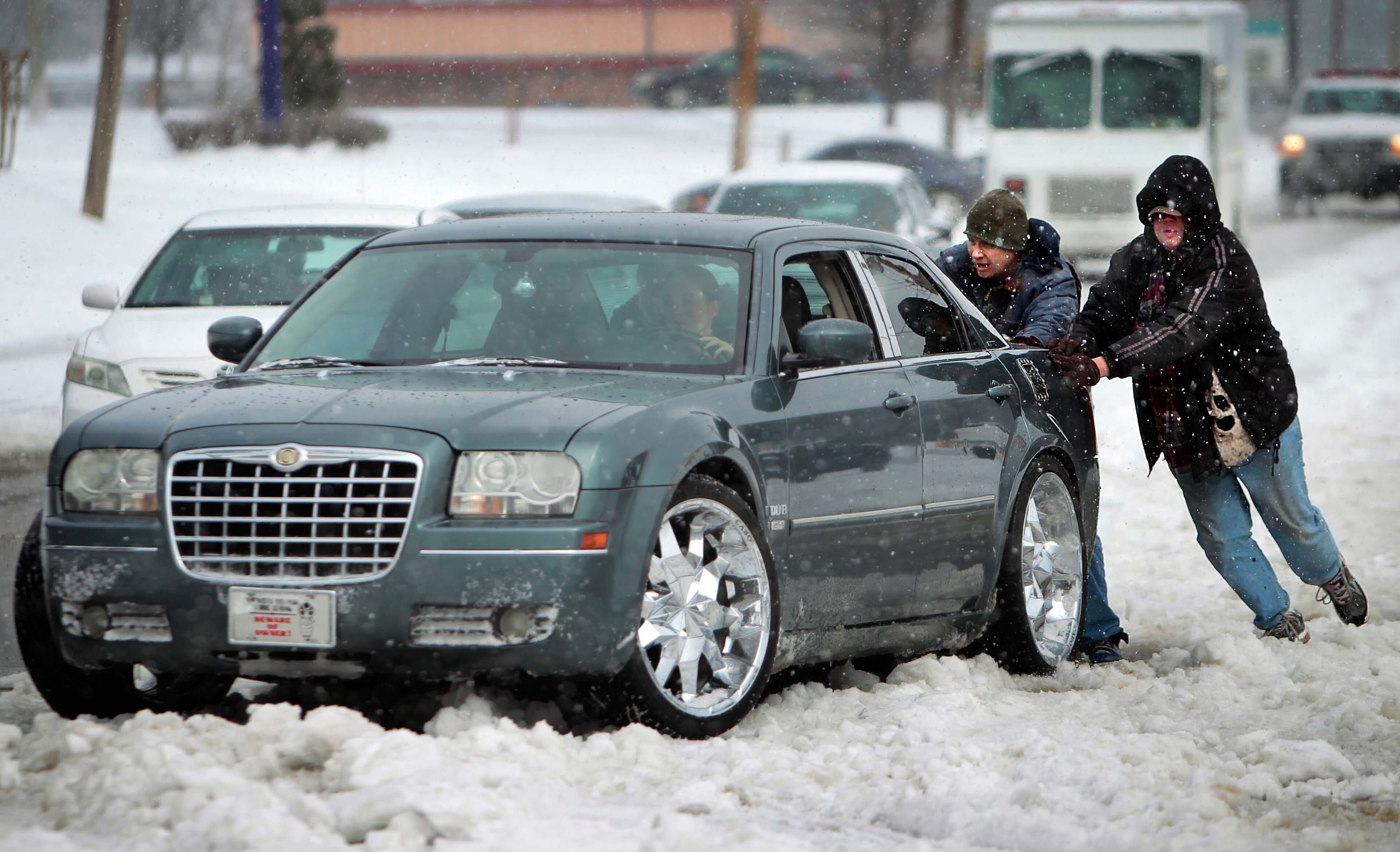 A group of people help push a stranded motorist out of a bank of snow in Frayser, Tenn., Monday, March 3, 2014 after a winter storm covered parts of Memphis in a blanket of ice over night. (AP Photo/The Commercial Appeal, Jim Weber)