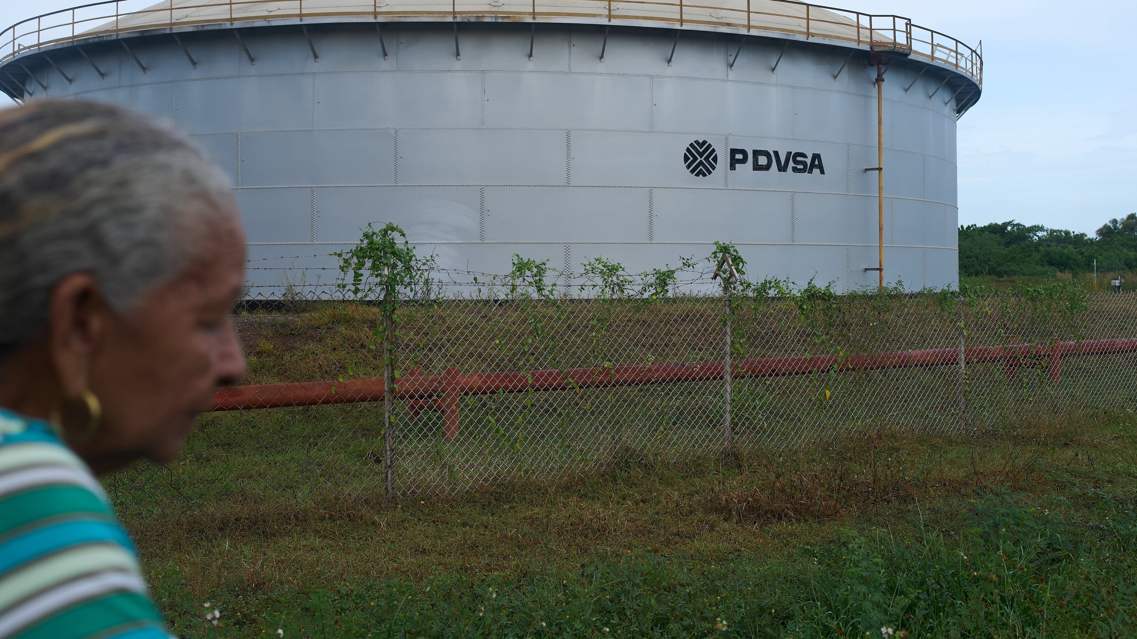 A woman walks near of a oil storage tank of Venezuela's state-run oil company, PDVSA in Cabimas, Venezuela, Tuesday, Sep. 1, 2026. (AP Photo/Ariana Cubillos)