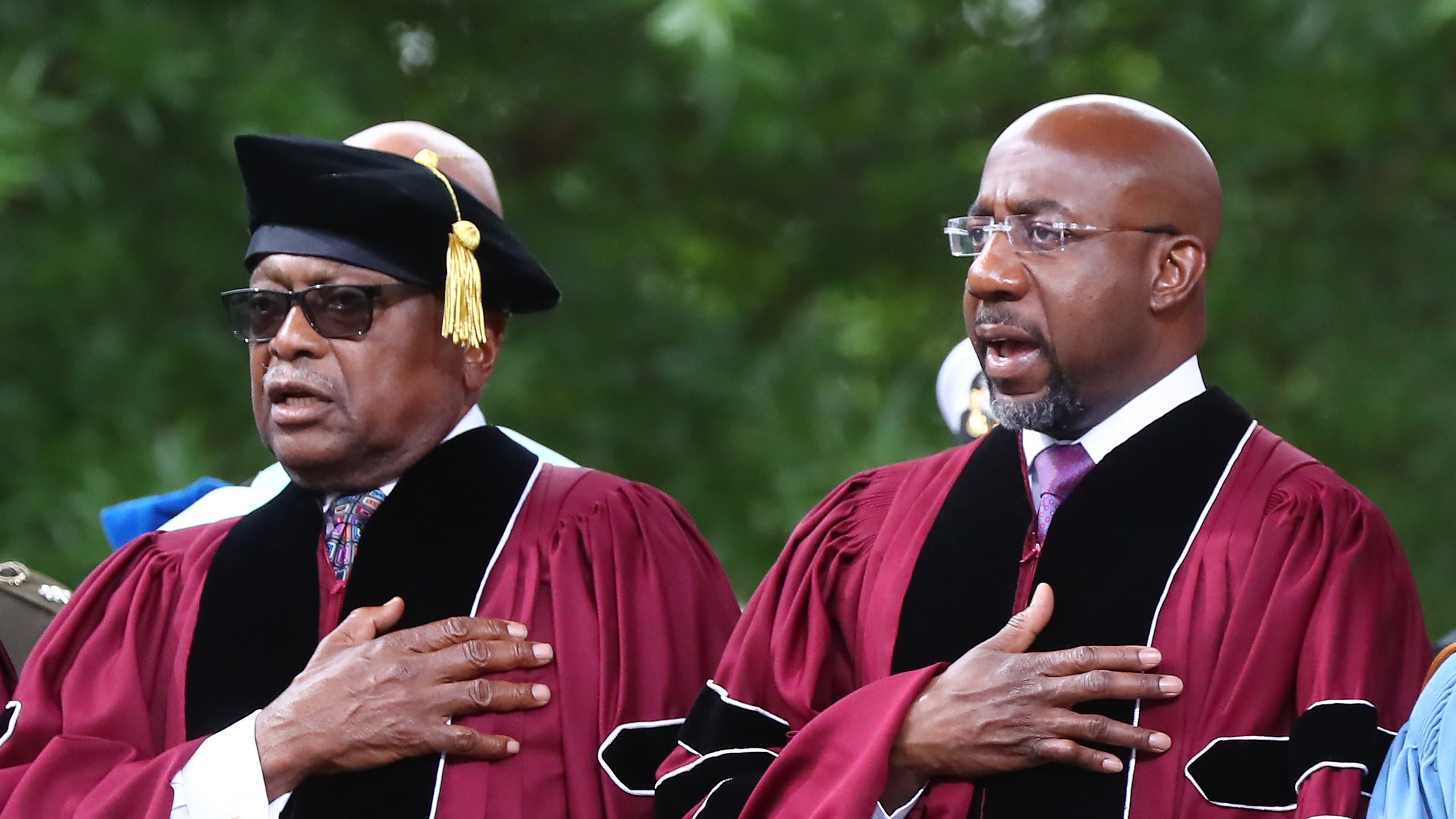 Rep. James E. Clyburn (left) of South Carolina, who received the Honorary Doctor of Laws degree, and Sen. Raphael G. Warnock (right), of Georgia, who received the Honorary Doctor of Humane Letters degree and also deliverd the commencement address, put their hands on their hearts for the presentation of colors and "The Star-Spangled Banner" during the Morehouse College 138th Commencement Ceremony on Sunday, May 15, 2022, in Atlanta. (Curtis Compton/AJC)