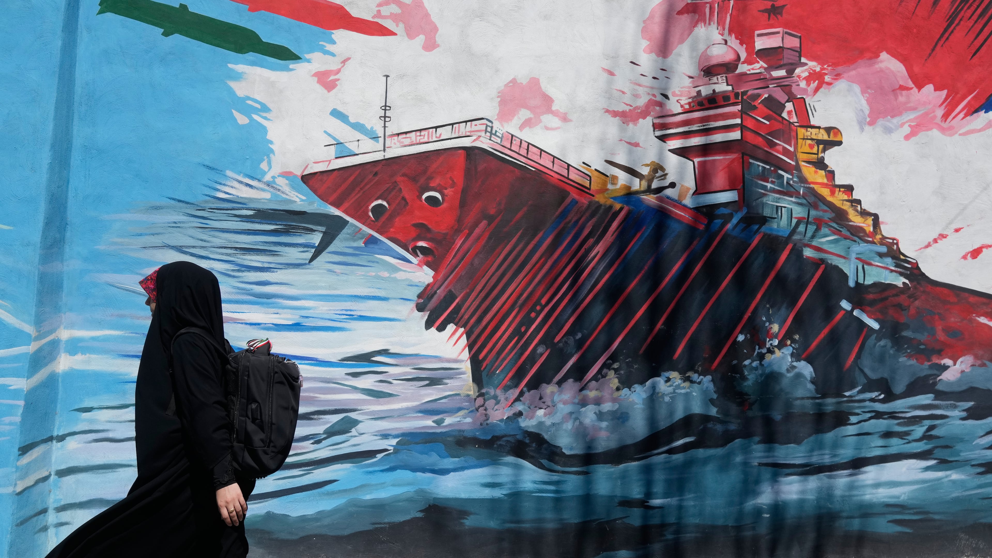 A woman walks past a mural depicting a U.S. aircraft carrier under missile attack in downtown Tehran, Iran, Monday, June 8, 2026. (AP Photo/Vahid Salemi)