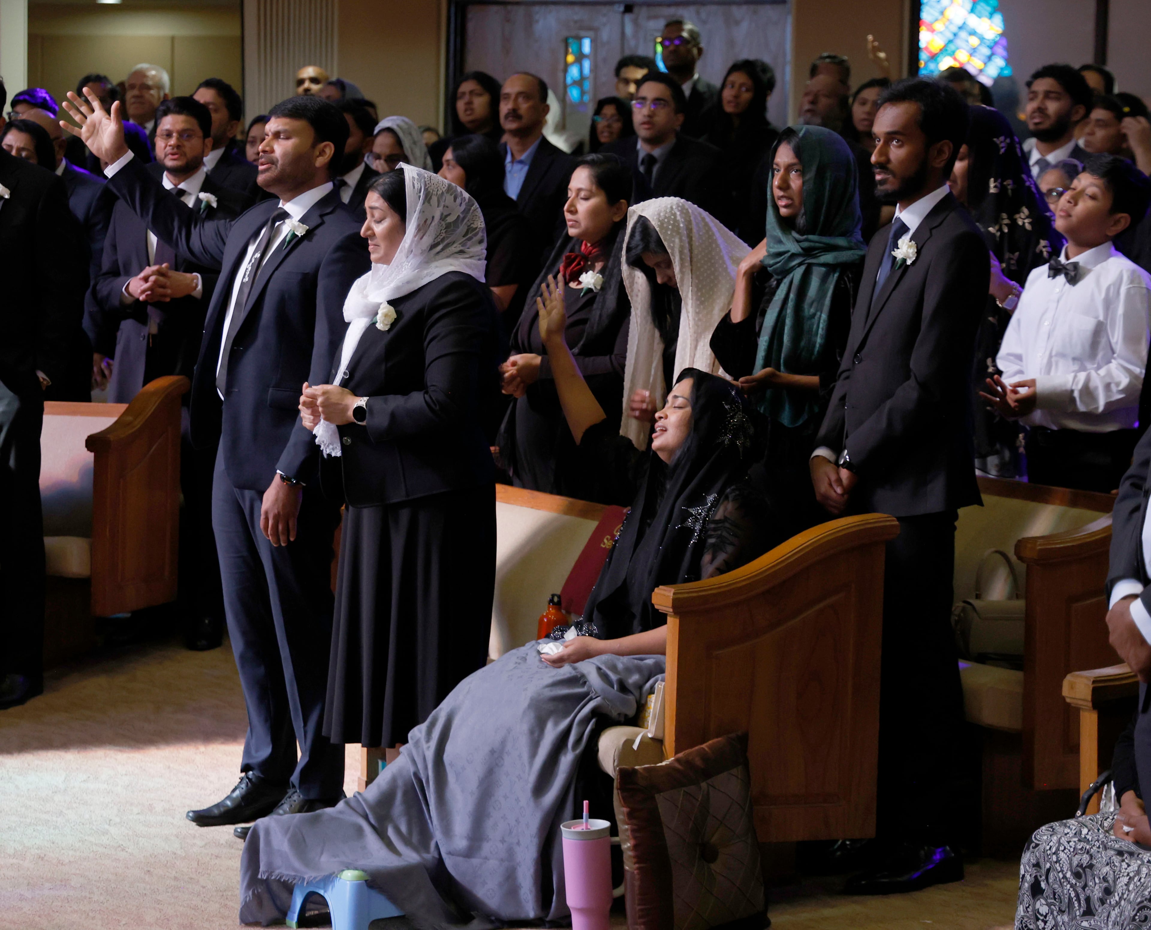 Dave Fiji's father and mother (front center) stand for a song during their son's funeral. Fiji's wife, Jesni Sam, elevates her foot on a stool. (Akili-Casundria Ramsess for the AJC)