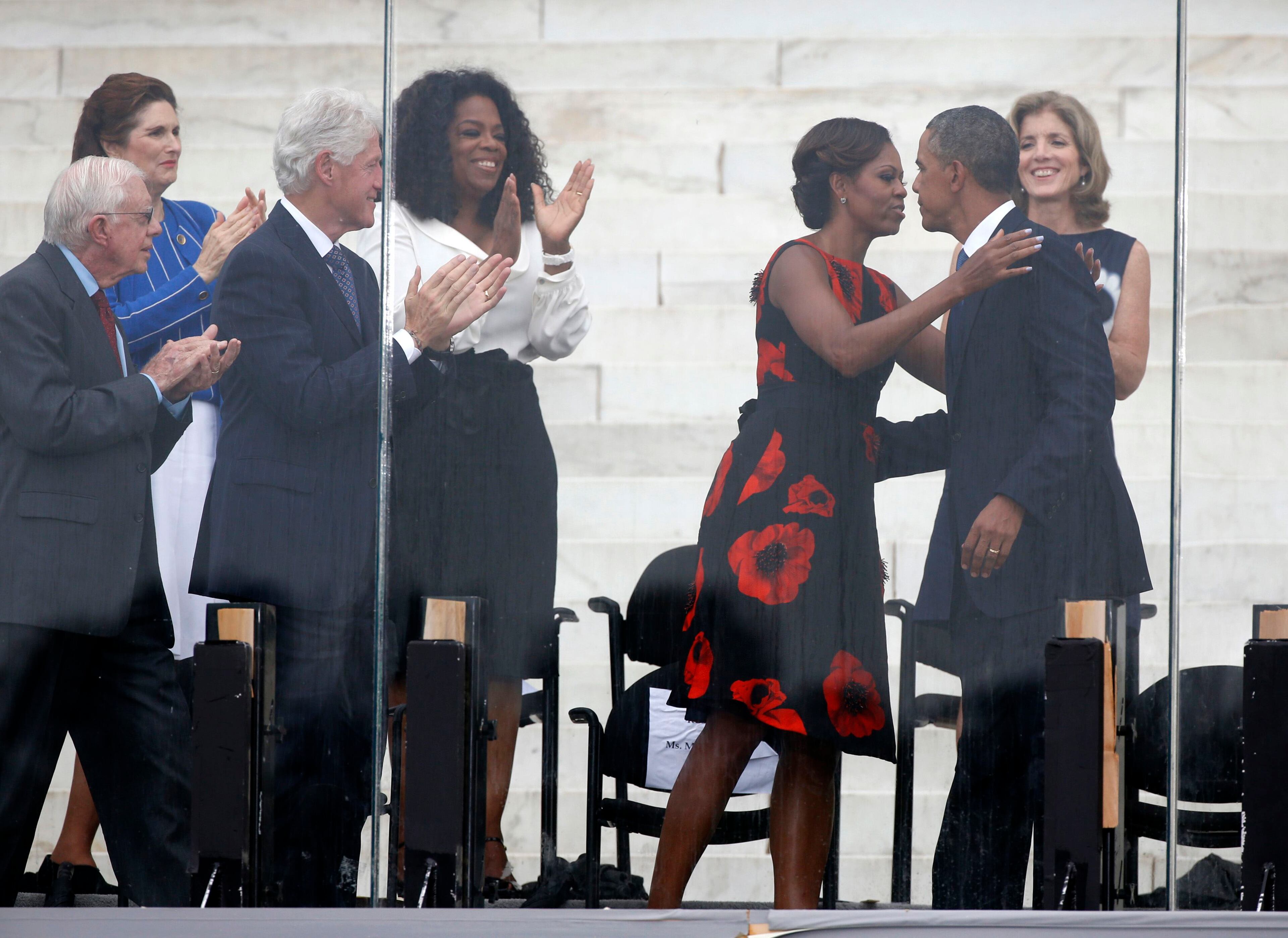U.S. first lady Michelle Obama (3rd R) kisses U.S. President Barack Obama (2nd R) following his remarks during a ceremony marking the 50th anniversary of Martin Luther King Jr.'s "I have a dream" speech on the steps of the Lincoln Memorial in Washington, August 28, 2013. Also pictured are (L-R) former U.S. president Jimmy Carter, former president Bill Clinton, talk show host Oprah Winfrey and Caroline Kennedy. Picture is taken through bullet-proof glass. REUTERS/Jason Reed (UNITED STATES - Tags: POLITICS ANNIVERSARY)