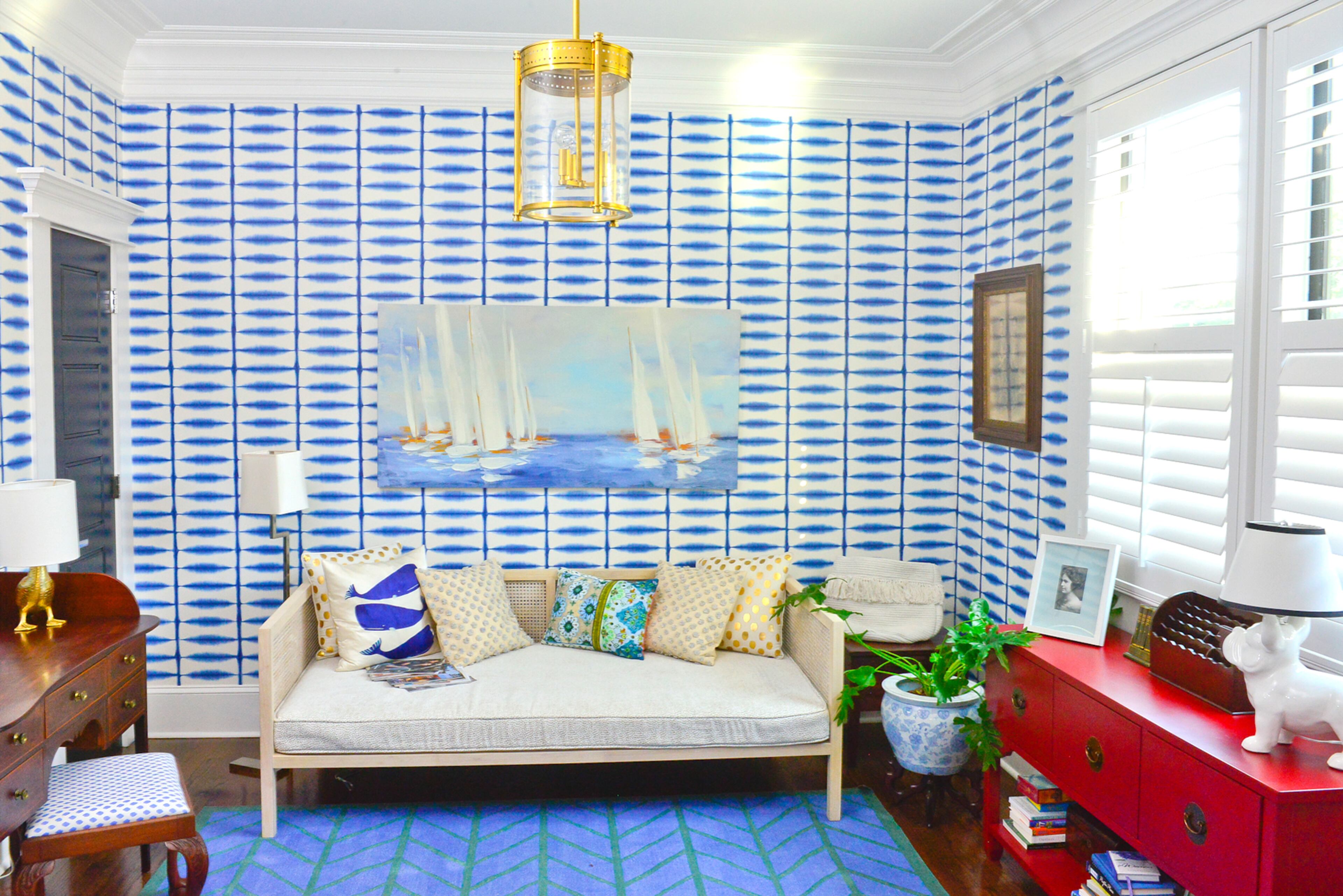 A daybed from CB2 is fitted with a custom-made mattress cover by Melissa Barraza, owner of M Squared Sewing. Coastal blues dominate the office's color scheme, from the large sailboat artwork and bright wallpaper to the blue-and-green Serena & Lily rug that anchors the space.