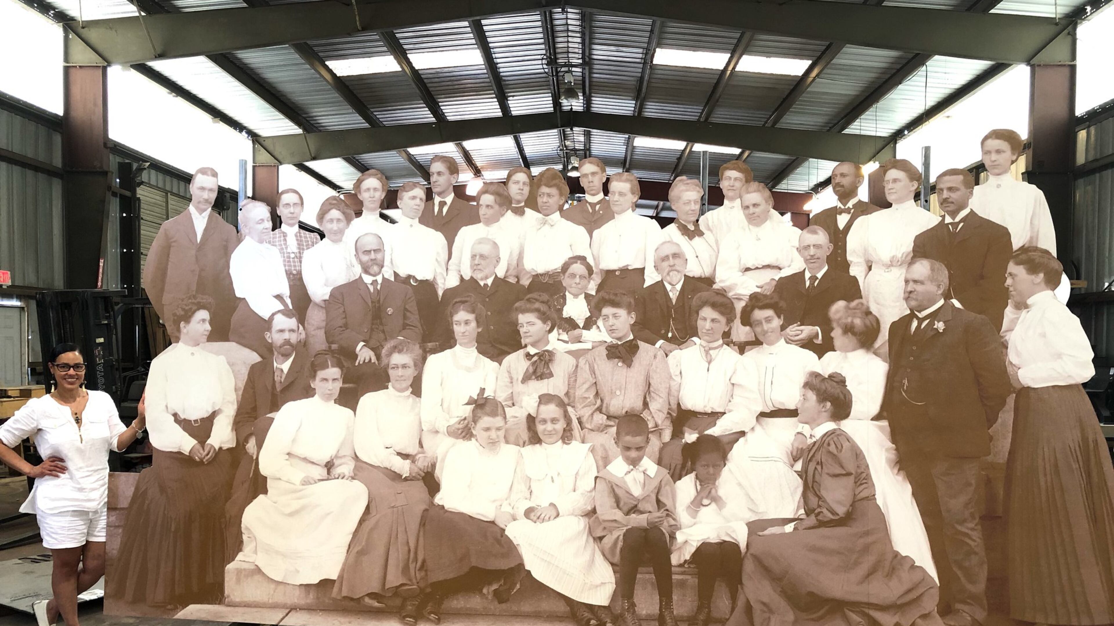 Atlanta Historian Karcheik Sims-Alvarado (standing lower left) stands behind the massive 17x8 reproduction of the turn of the 20th century photograph of the Atlanta University faculty. The photo includes, W.E.B. Du Bois (last man on the top row to the right); Alonzo Herndon (top row on the left); Atlanta University President Horace Bumstead (middle row with beard wearing a chain on his vest)