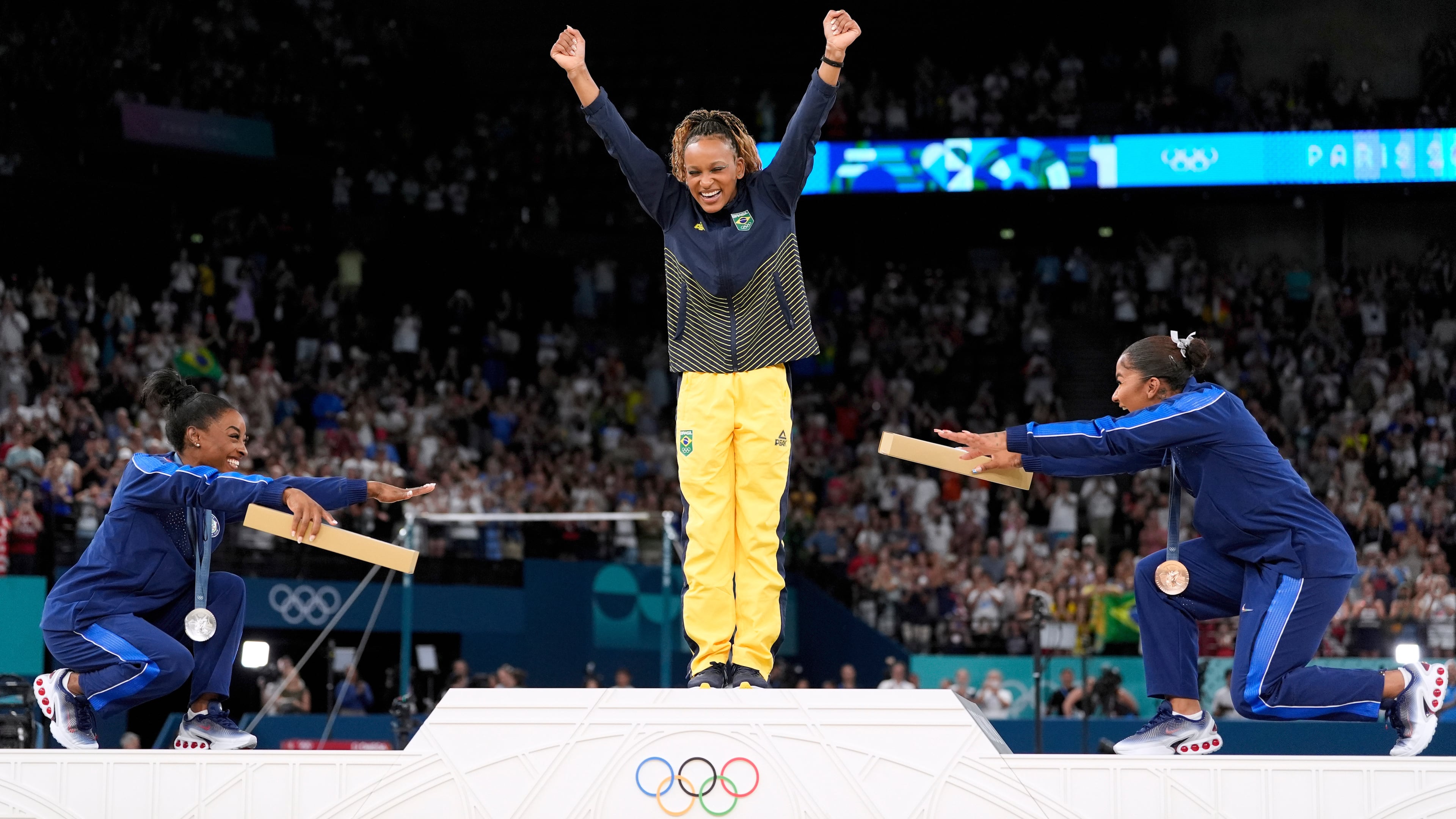 FILE - Silver medalist Simone Biles, of the United States, left, and bronze medalist Jordan Chiles, of the United States, right, bow to gold medalist Rebeca Andrade, of Brazil, during the medal ceremony for the women's artistic gymnastics individual floor finals at Bercy Arena at the 2024 Summer Olympics, Aug. 5, 2024, in Paris, France. (AP Photo/Abbie Parr, File)