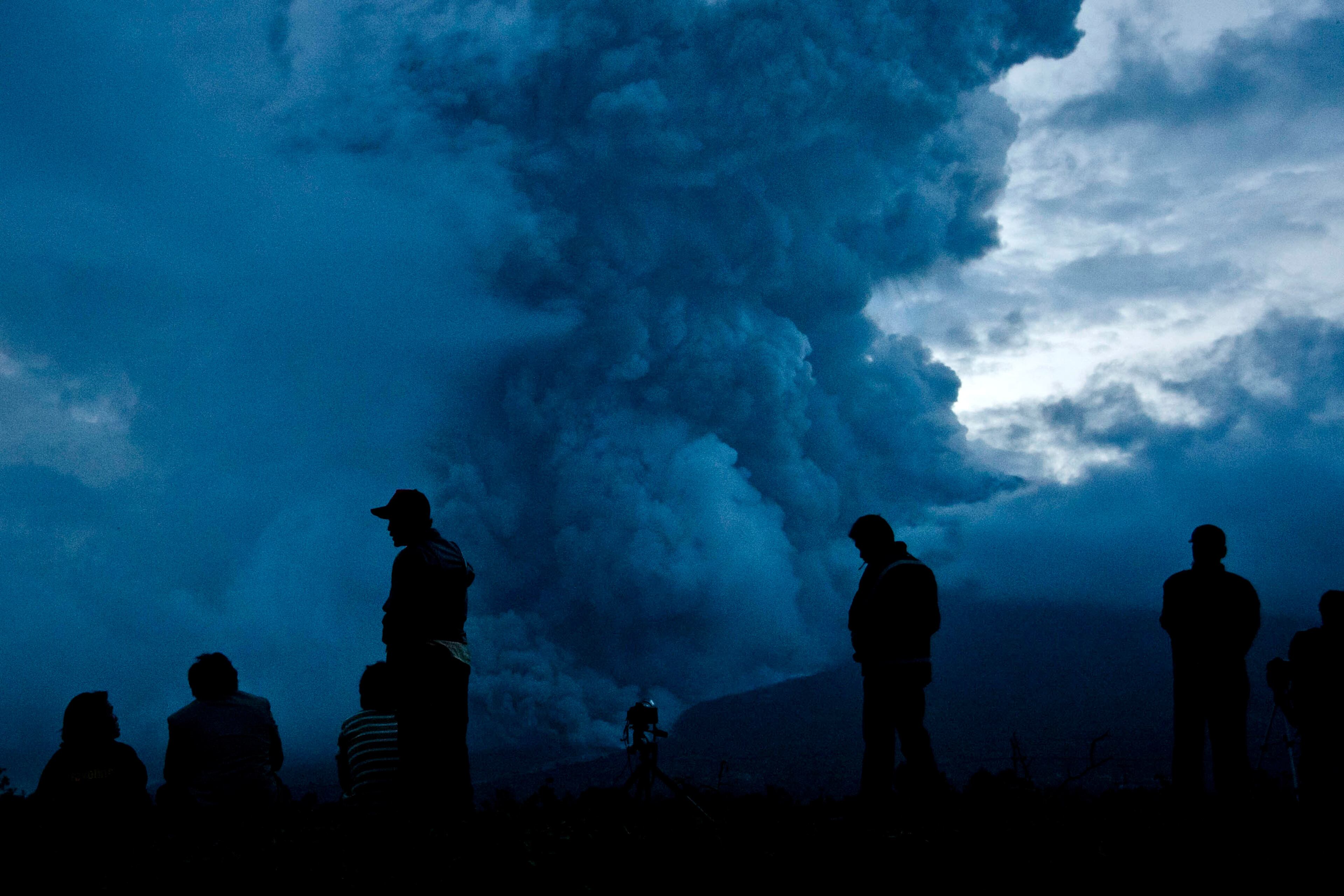 People watch as Mount Sinabung spews pyroclastic smoke on January 3, 2014 in Karo District, North Sumatra, Indonesia. The number of displaced persons has increased to 19,000 in Western Indonesia as Mount Sinabung continues to spew ash and smoke after several eruptions since September. 11 deaths have now been recorded as a result of the eruptions with hundreds more falling ill. Officials expect the number of evacuees to rise as volcanic activity remains high.