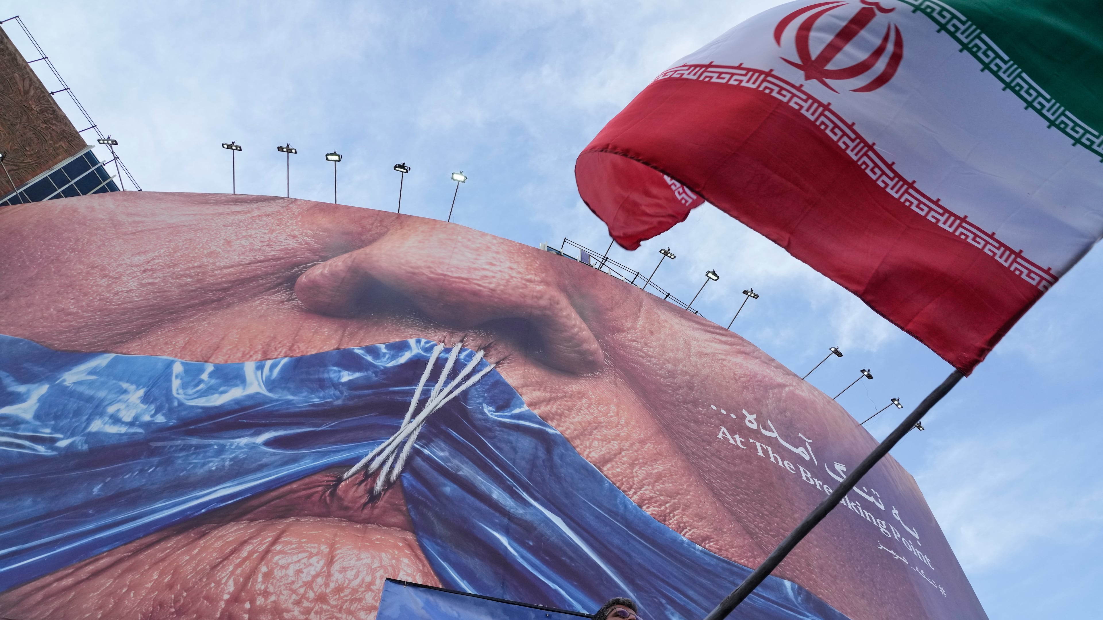 A man waves an Iranian flag for a pro-government campaign under a billboard with graphic showing Strait of Hormuz and sewn lips of U.S. President Donald Trump in a square in downtown Tehran, Iran, Wednesday, May 6, 2026. (AP Photo/Vahid Salemi)