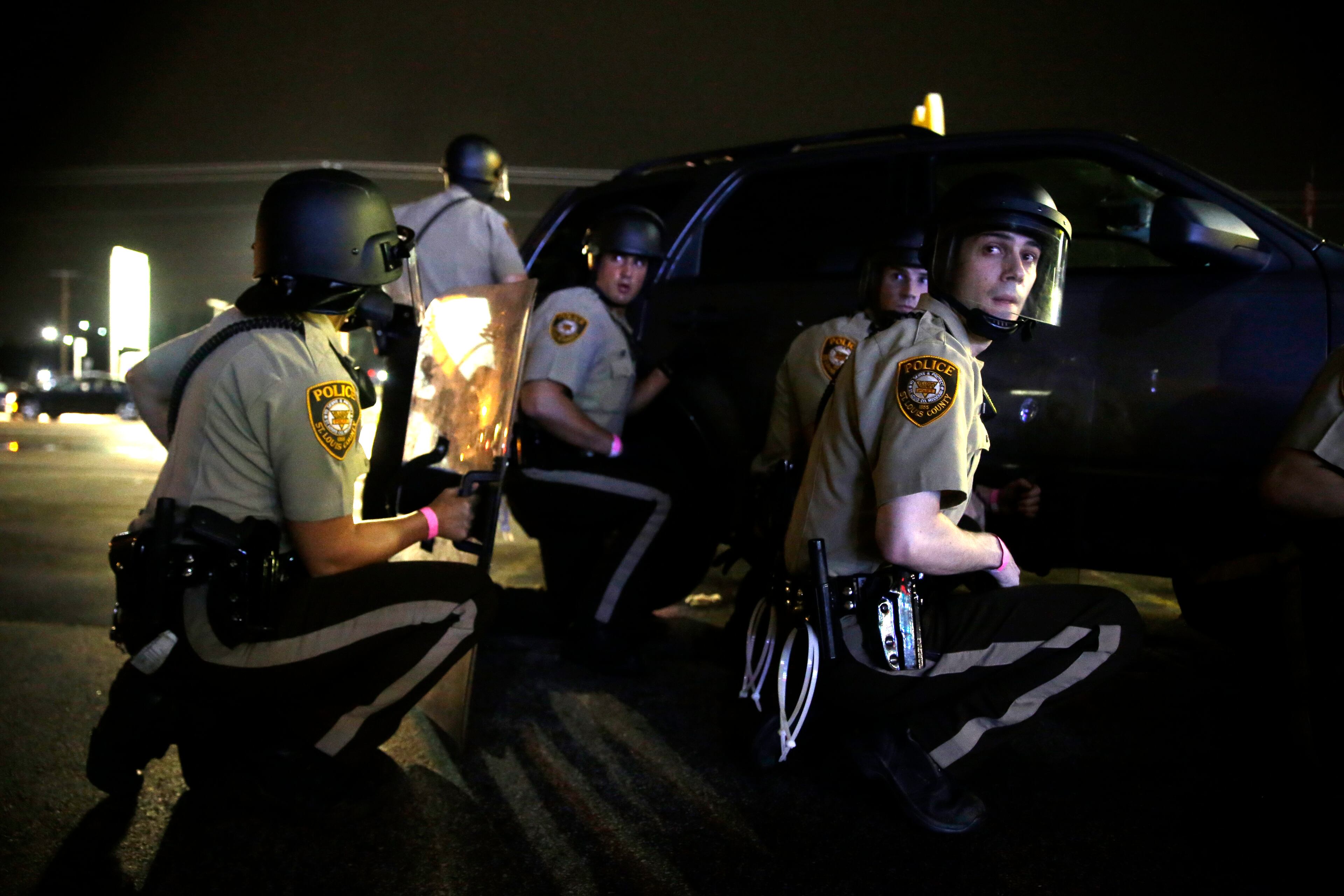 Police take cover behind a vehicle during a protest in Ferguson, Mo., Sunday, Aug. 9, 2015. The one-year anniversary of Michael Brown's death in Ferguson began with a march in his honor and ended with a protest that was interrupted by gunfire. (AP Photo/Jeff Roberson)