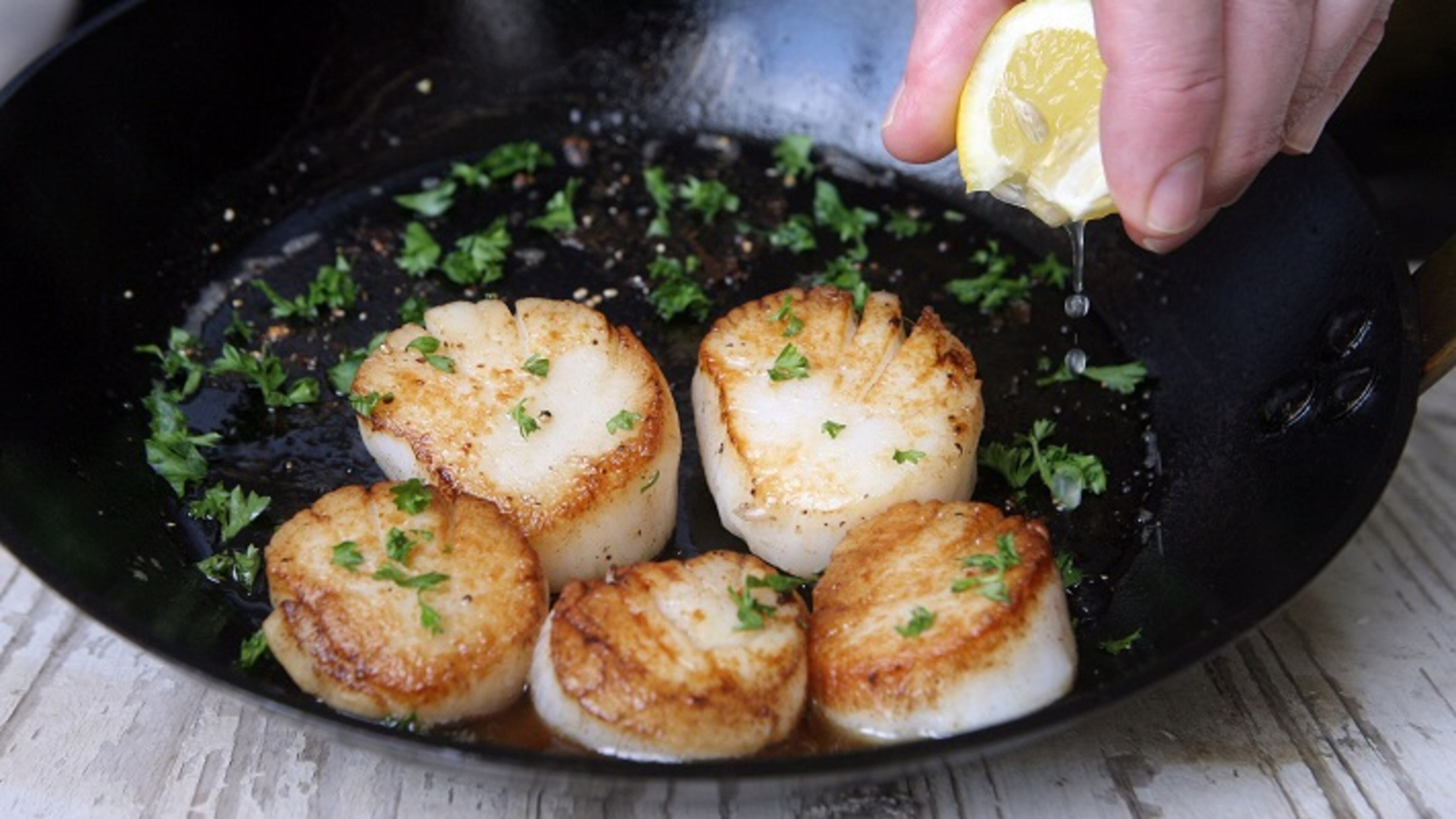 Squeeze a bit of lemon on seared scallops in the pan with butter and parsley garnish. (Hillary Levin/St. Louis Post-Dispatch/TNS)