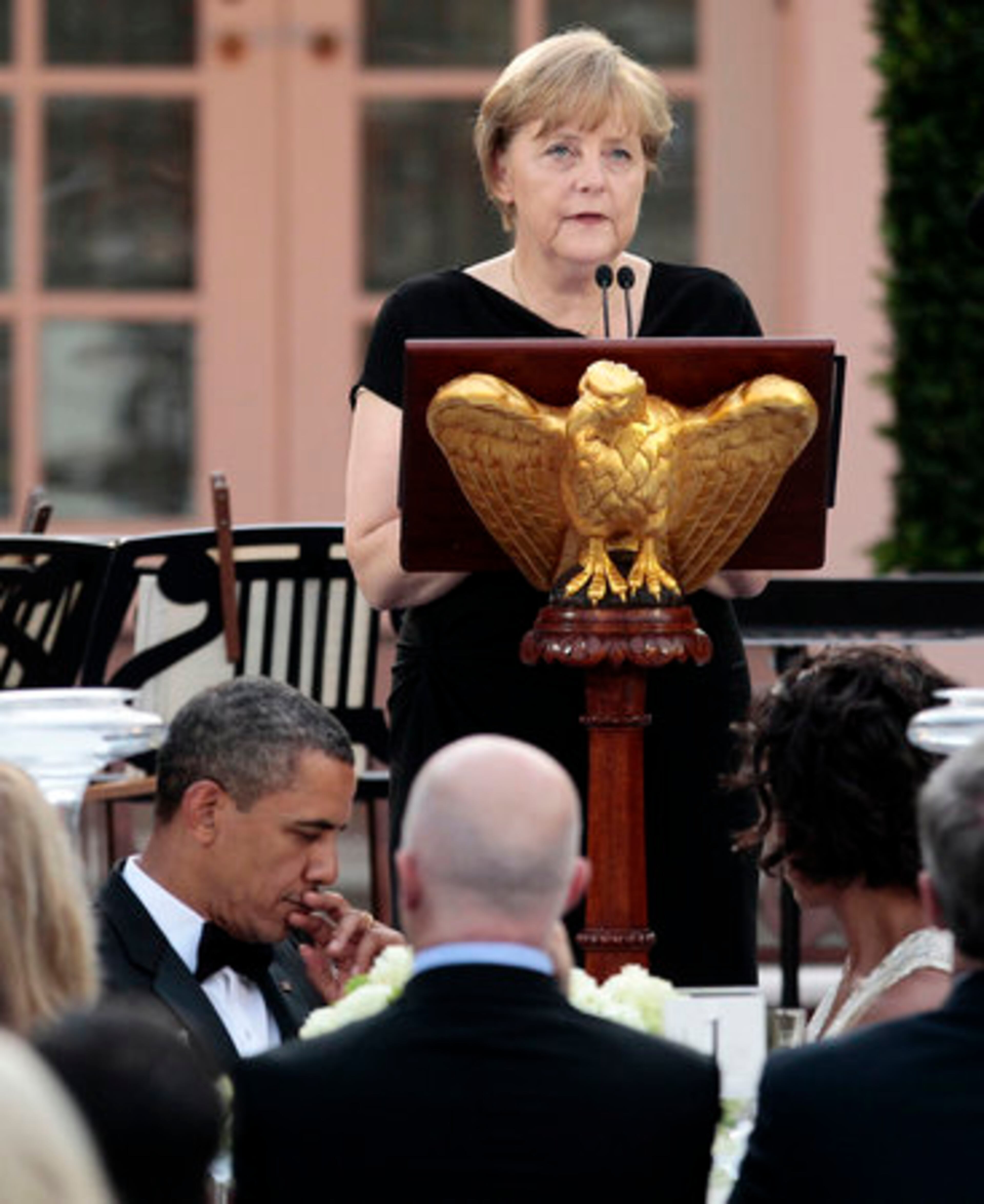 President Barack Obama, left seated, listens to German Chancellor Angela Merkel speak, after she received the Medal of Freedom during the State Dinner in the Rose Garden of the White House in Washington, Tuesday, June 7, 2011.