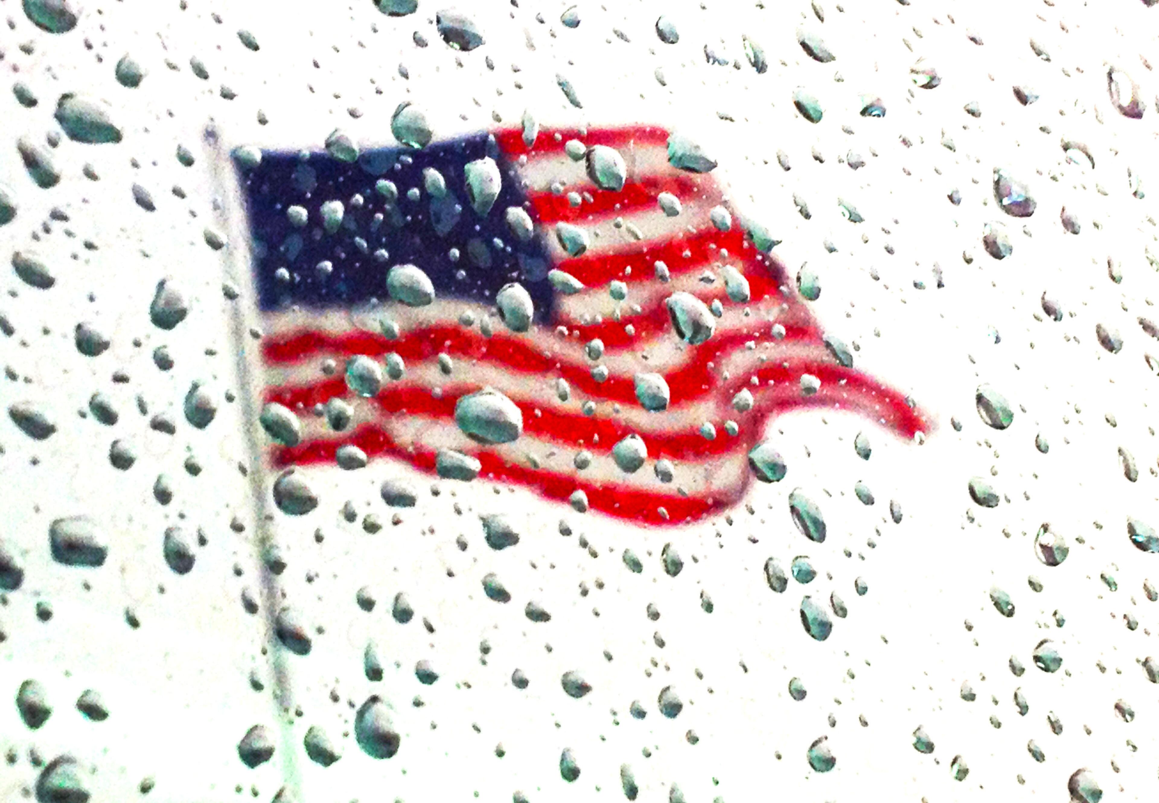 The American flag is reflected on a rain drop coated windshield at a car dealership on 59 south in Houston, Texas, Wednesday, May 15, 2013.