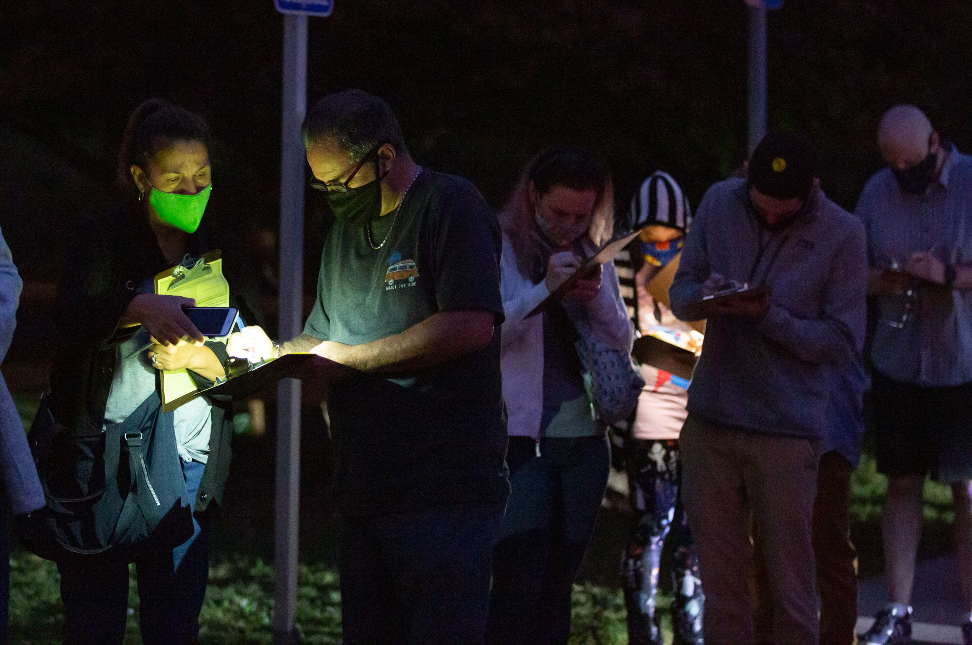 People fill out forms by the light of their phones while waiting in line to vote at Shorty Howell Park in Gwinnett on Saturday, October 24, 2020. STEVE SCHAEFER / SPECIAL TO THE AJC