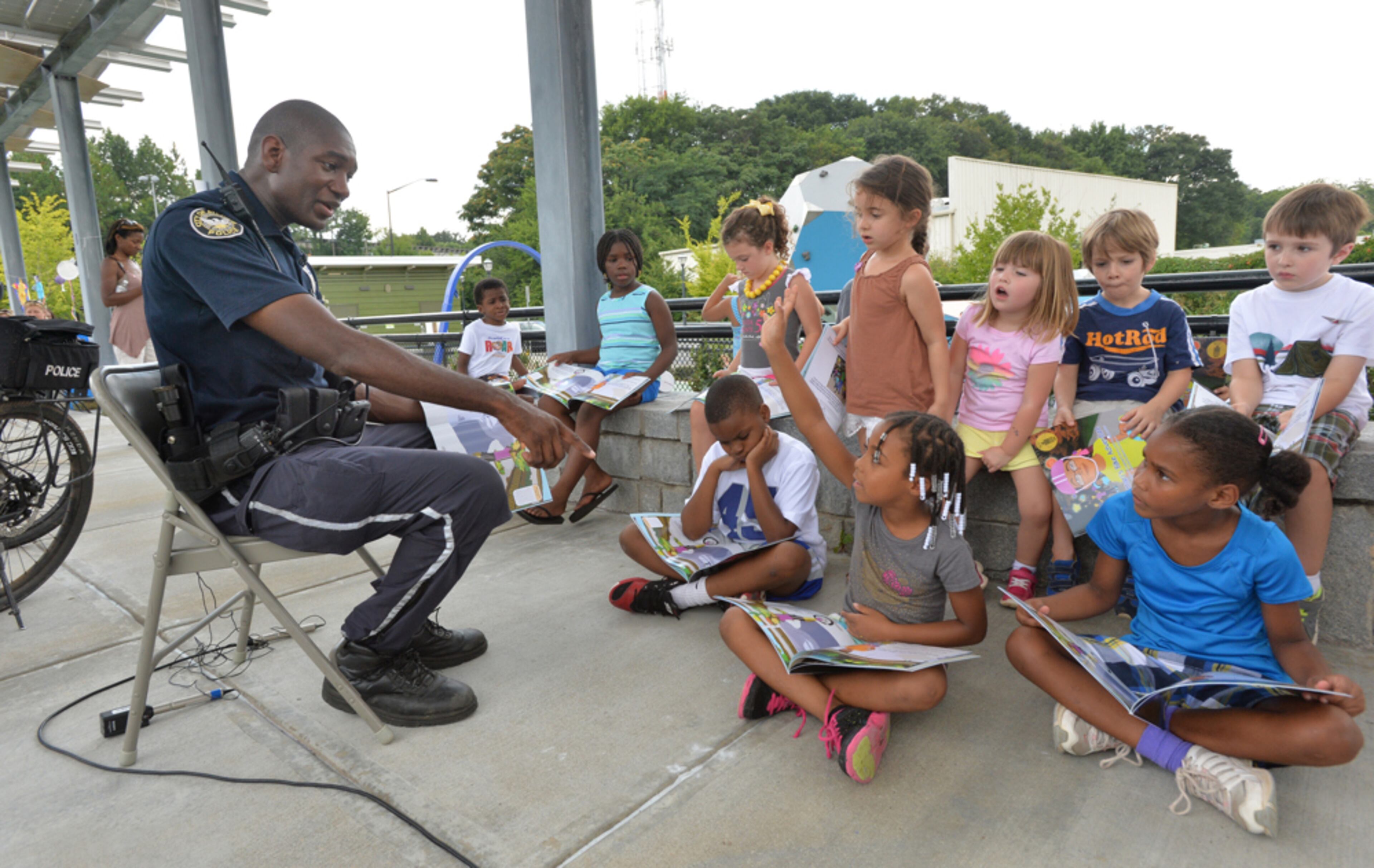 READING IS A RIGHT--July 23, 2014 Atlanta - Ialiyah Bennett, 8, raises her hand to answer a question as officer Michael Walker (left) reads the book, Amari's Bike Adventure, at Historic Fourth Ward Skate Park near the Atlanta Beltline on Wednesday, July 23, 2014. The Atlanta Police Department is participating in the Mayor's Summer Reading Club and hosts two readings along the Atlanta Beltline. As a part of reading program, officers from the Atlanta Police Department's Path Force Unit read the book, Amari's Bike Adventure. The book follows the lead character Amari as she explores the Atlanta Beltline and meets several helpful people including an Atlanta Police Path Force Officer. HYOSUB SHIN / HSHIN@AJC.COM