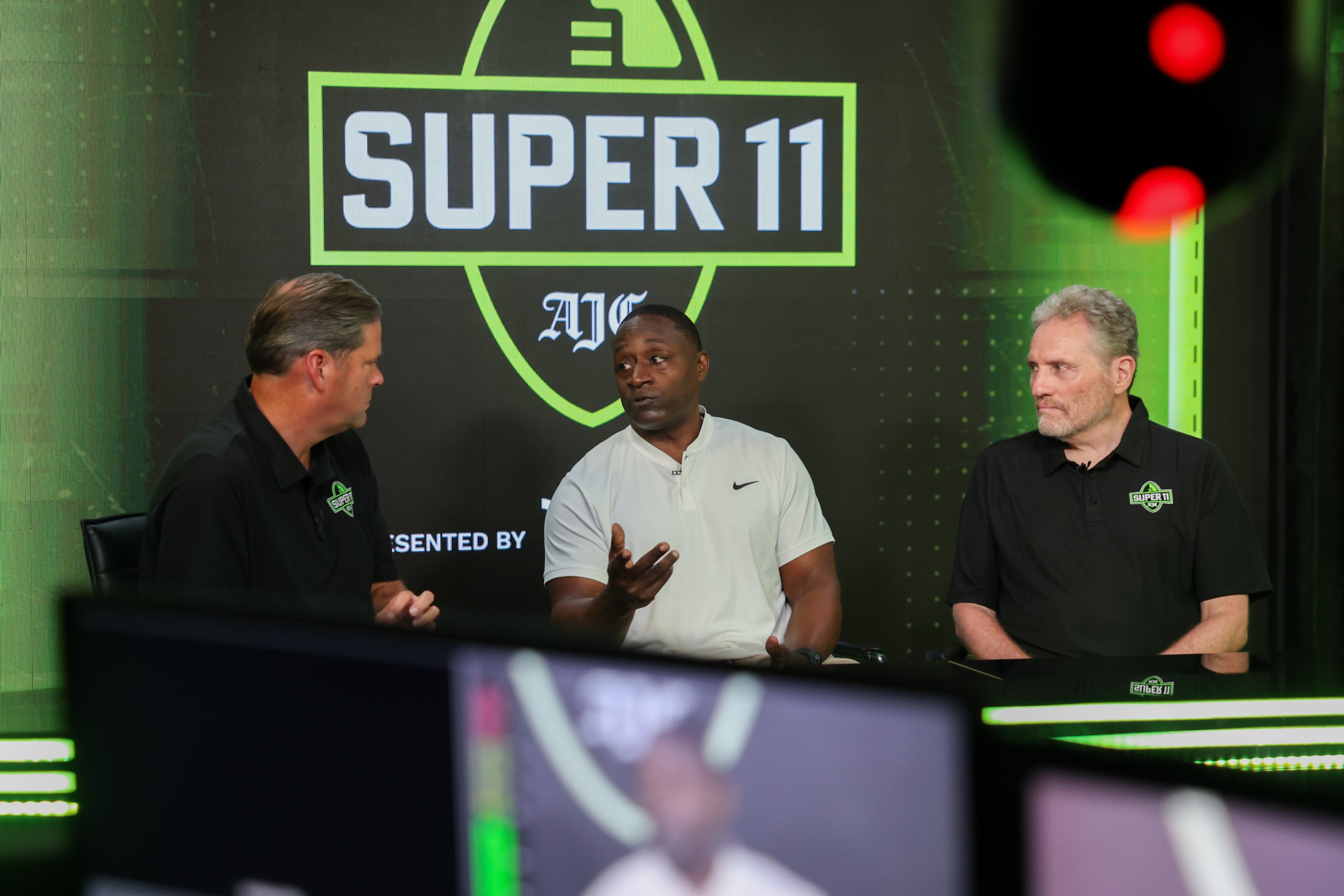 (L-R) DawgNation’s Brandon Adams appears with former Super 11 honoree Garrison Hearst and AJC’s Todd Holcomb during the taping of the Super 11 reveal show at Score ATL in Roswell on Aug. 3, 2026. (Arvin Temkar/AJC)