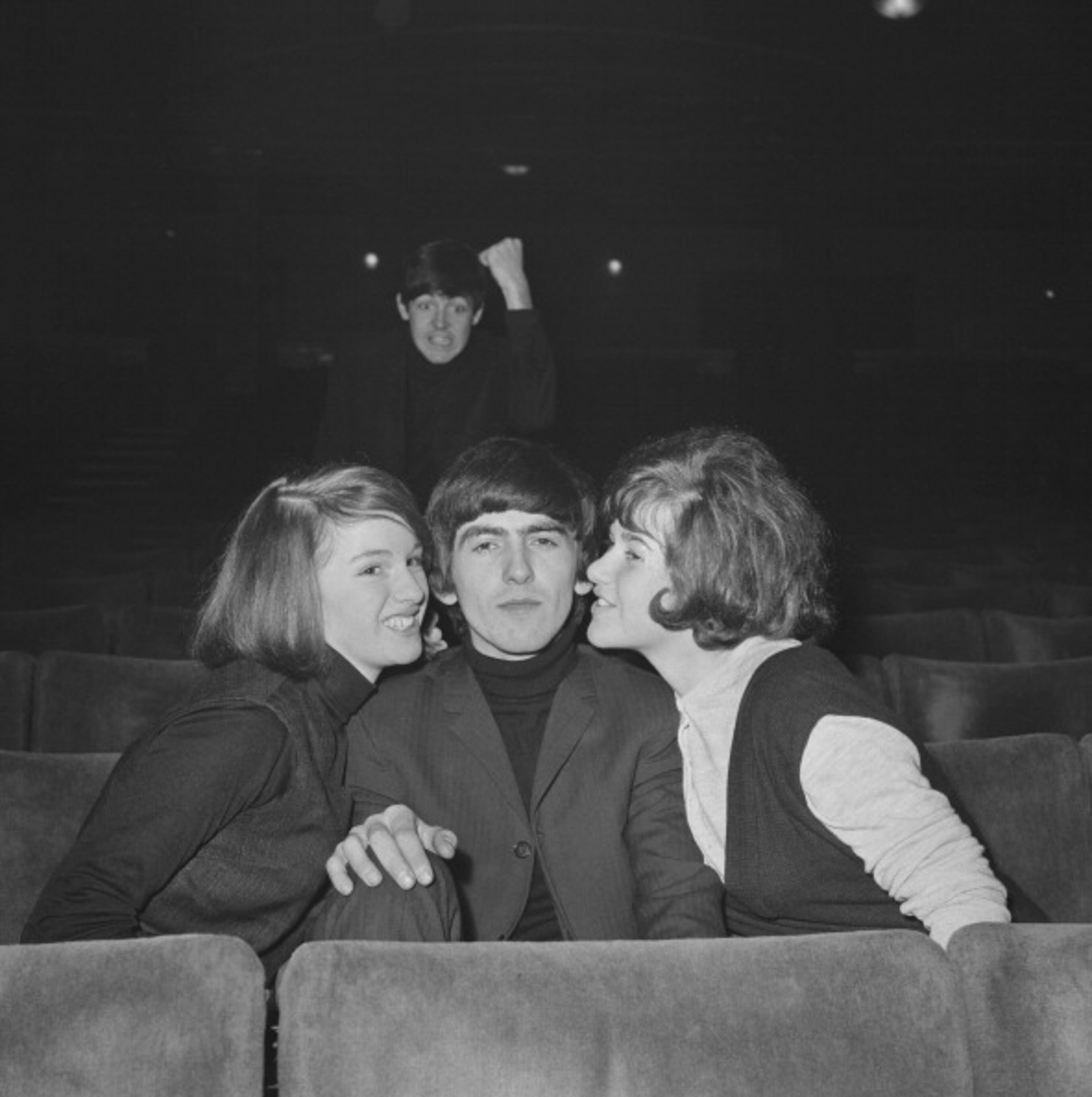 George Harrison (1943 - 2001) of The Beatles enjoys the attentions of two fans, as Paul McCartney shakes his fist in the background, at the Gaumont Cinema, Doncaster, 10th December 1963. (Photo by Mark and Colleen Hayward/Getty Images)