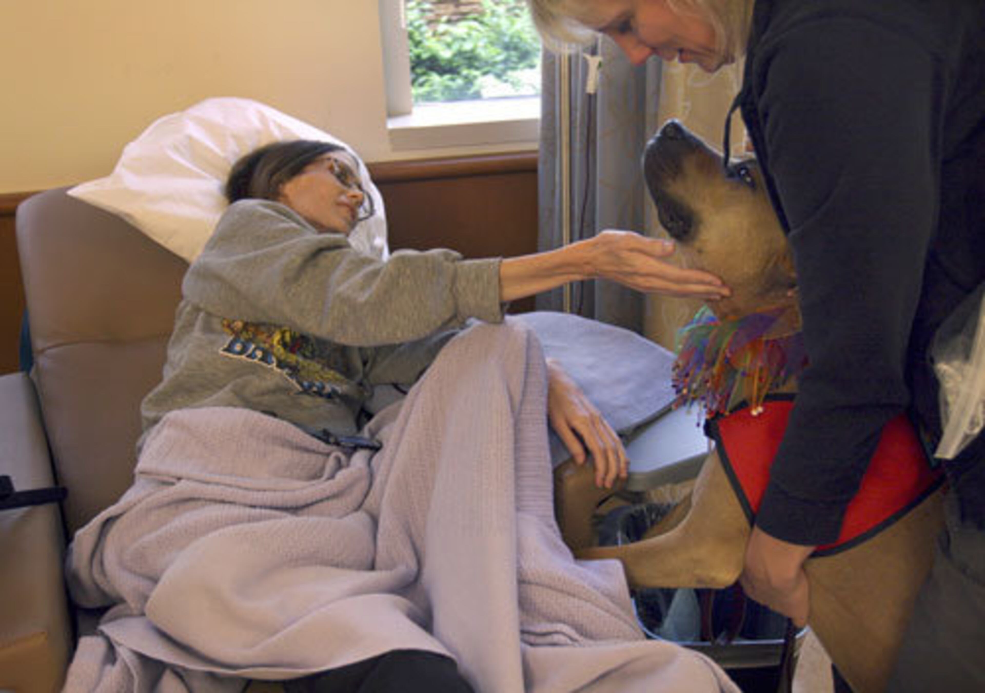 Leo, a certified therapy dog, visits client Tanya Olsen, left, at the Oncology and Hematology Infusion Therapy Center clinic in Mountain View, Calif. Marthina McClay, Leo's foster guardian, is at right.