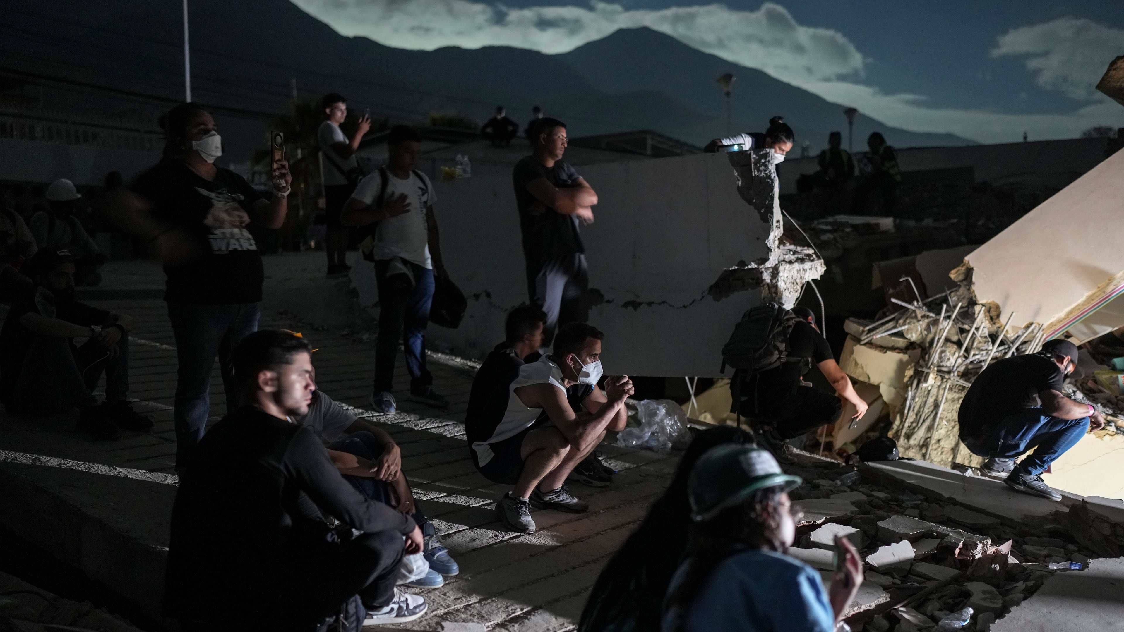 Residents watch rescuers' efforts to reach survivors beneath the rubble of a building that collapsed in the earthquakes in La Guaira, Venezuela, early Monday, June 29, 2026. (AP Photo/Matias Delacroix)