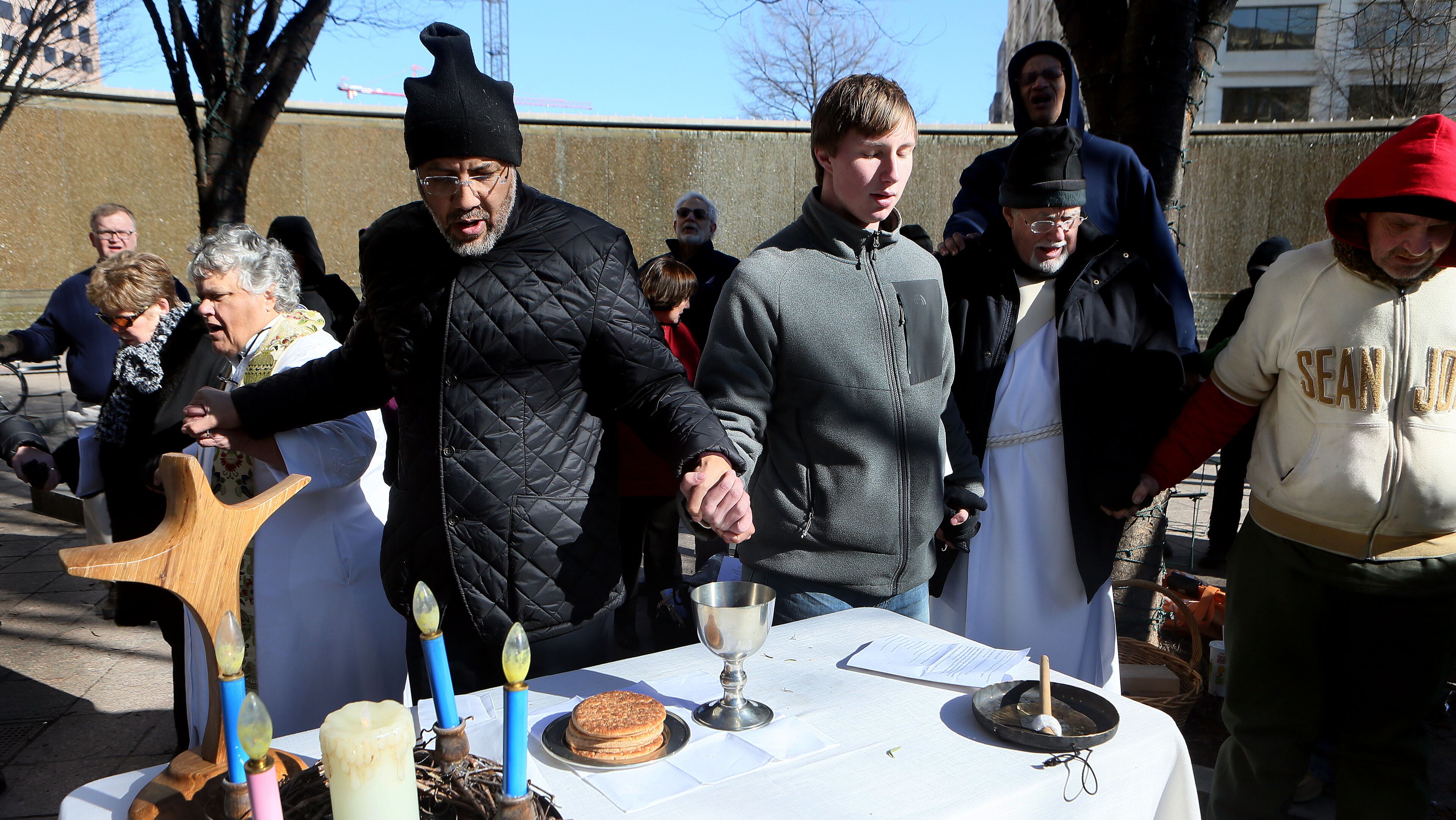 Bishop Robert Wright (center left in black cap) prayed as members of The Cathedral of St. Philip joined the Church the Common Ground to celebrate the Holy Eucharist with the homeless at Woodruff Park in downtown Atlanta on Tuesday, Dec. 24, 2013. The Church of the Common Ground, led by Rev. Mary Wetzel, has been meeting weekly for morning prayer at the downtown since 2006 averaging 45-50 people every Sunday. It is a worshiping community of the Episcopal Church in Middle and North Georgia (Diocese of Atlanta), which provides support for the spiritual, emotional and physical needs of unhoused men and women.