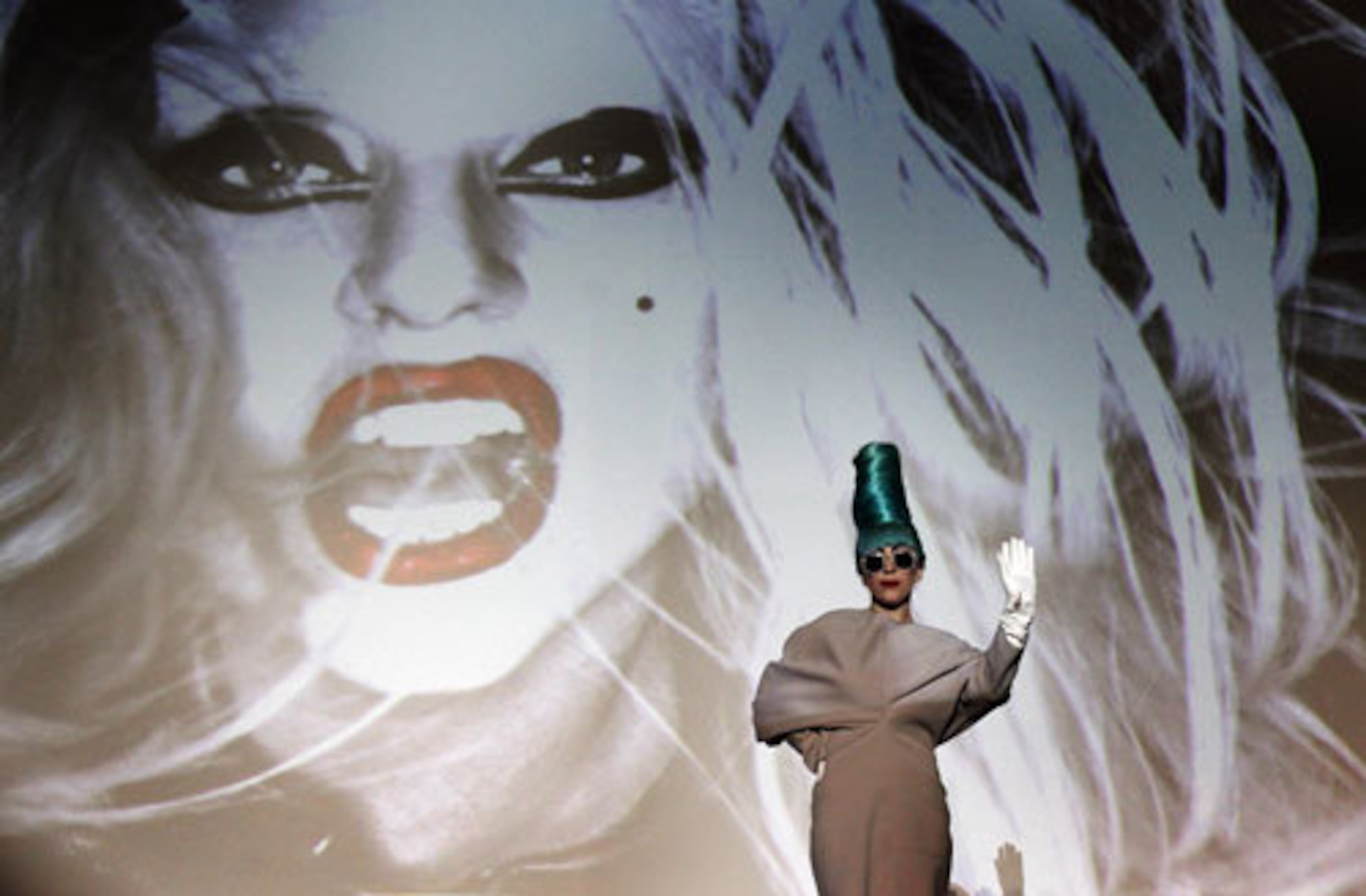 Lady Gaga stands in front of her image as she waves to members of the media.