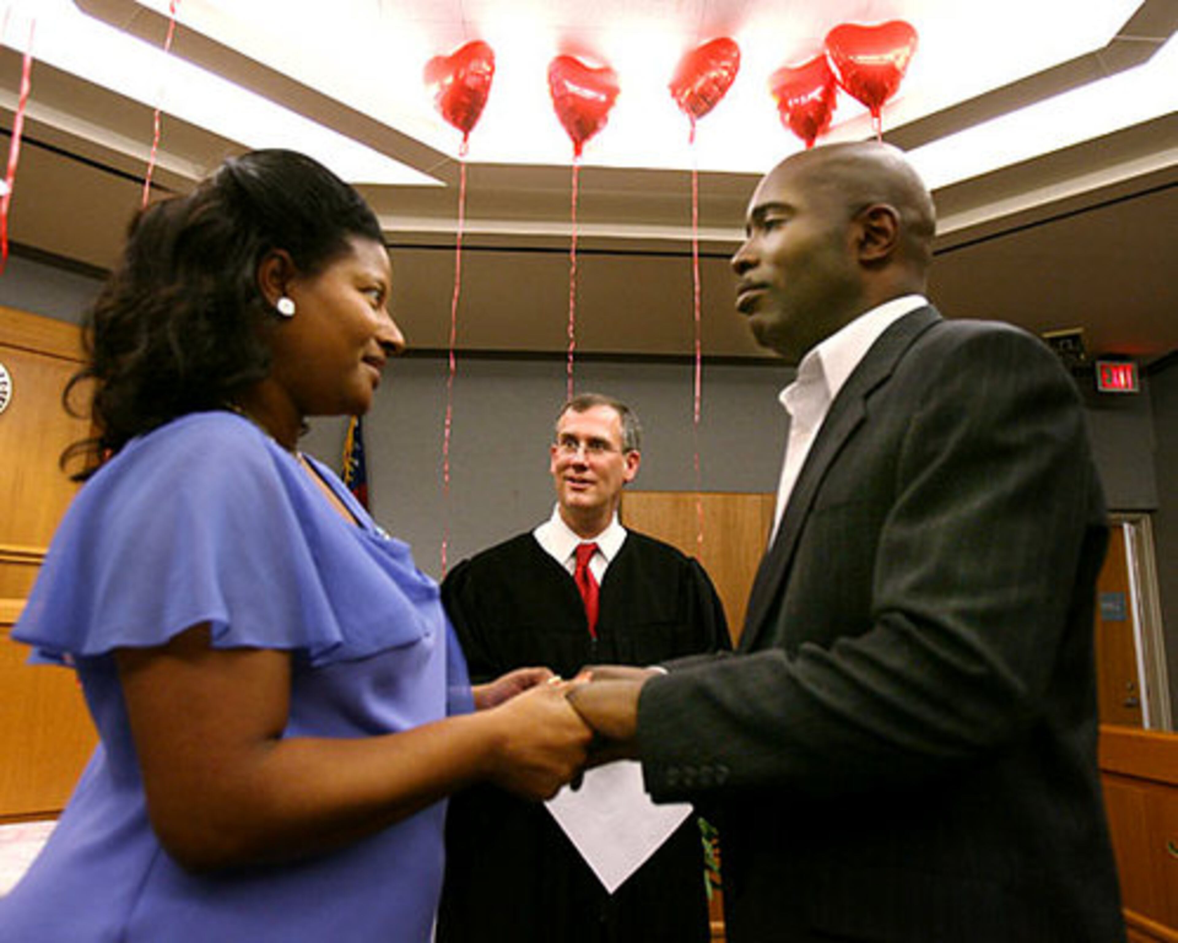 As heart-shaped baloons floated overhead, Chanetta Russell (left) recites her marriage vows to her fiance Adric Samuel, both of Suwanee, as their marriage is presided over by Gwinnett County Chief Magistrate Judge George Hutchinson, III (center), for the Gwinnett County Magistrate Court's traditional annual Valentine's Day free marriages and vow renewal ceremonies.