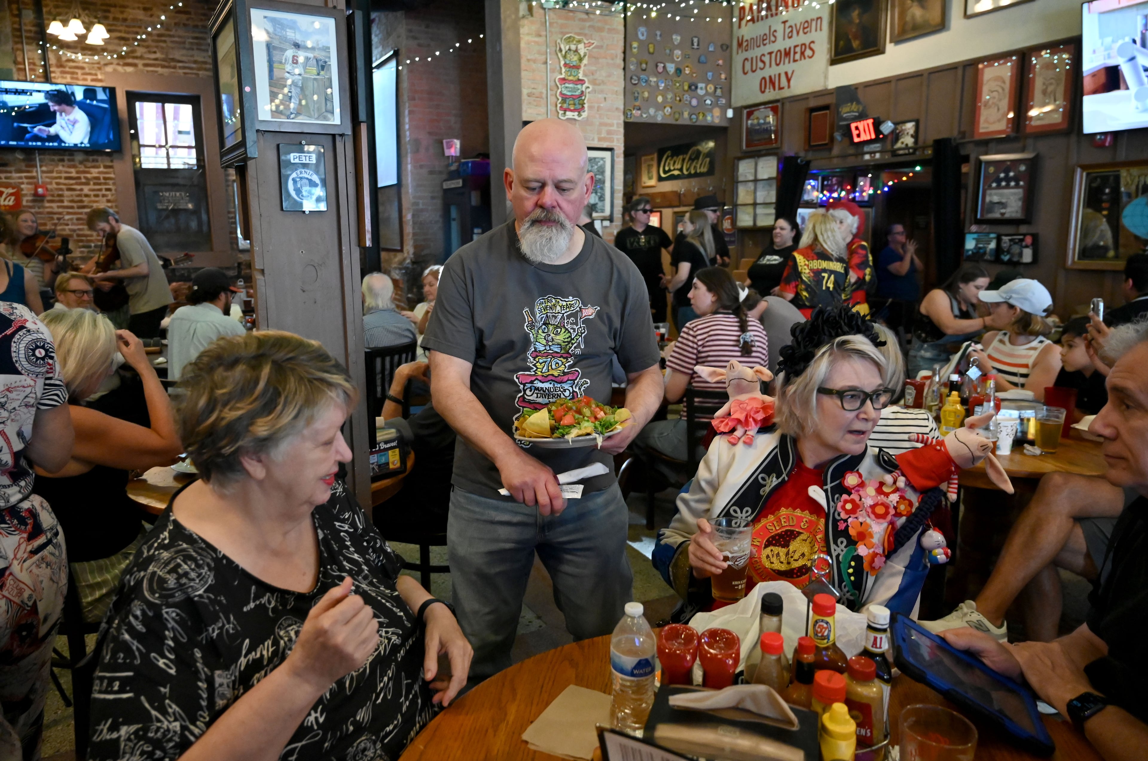 General manager Steve Pitts (center, standing) assists customers during Manuel’s Tavern’s 70th anniversary celebration. (Hyosub Shin/AJC)