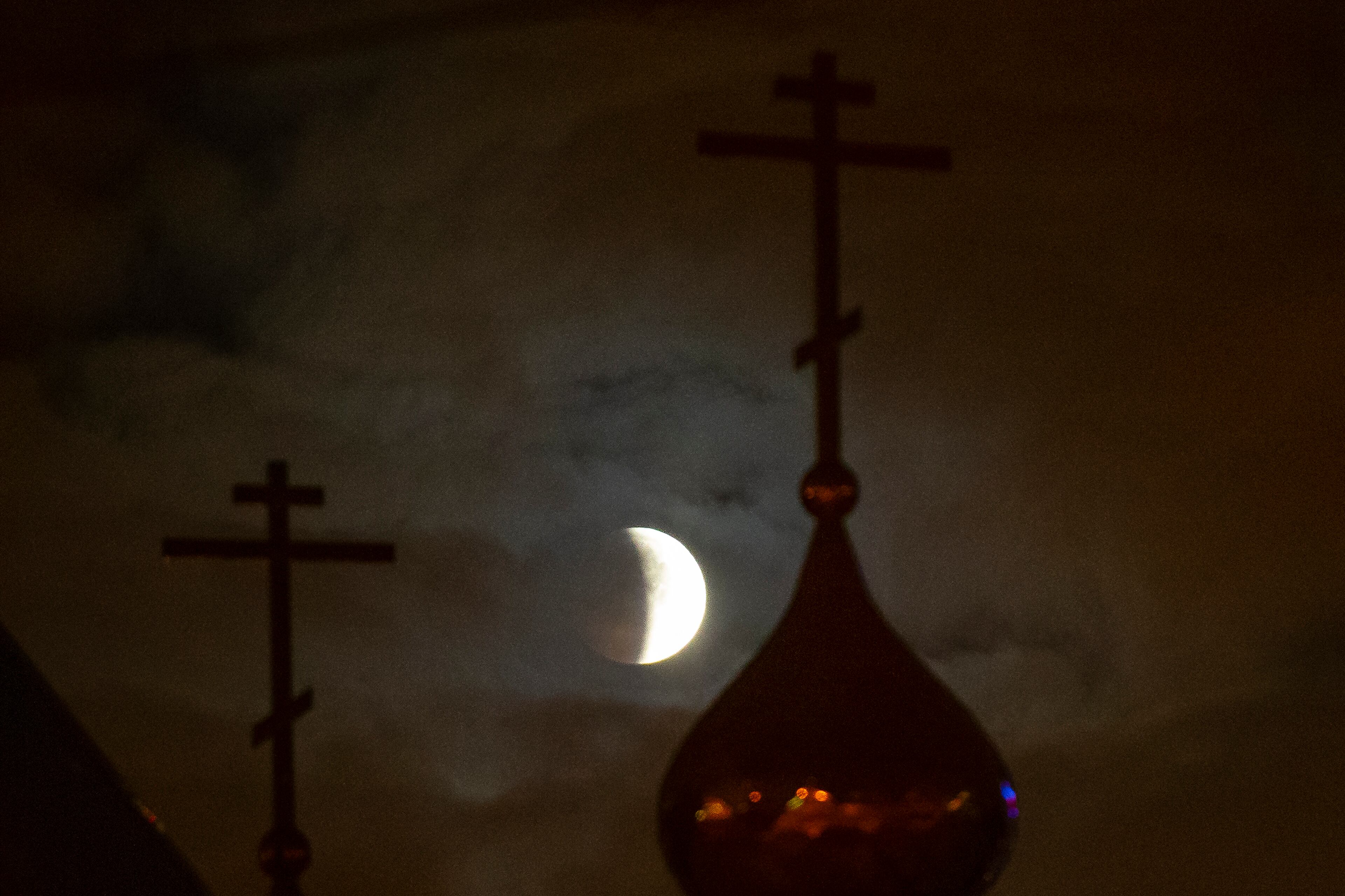 A lunar eclipse progresses behind a Russian Orthodox Church in Moscow, Russia, Monday, Jan. 21, 2019. The eclipse takes place when the full moon is at or near the closest point in its orbit to Earth, a time popularly known as a supermoon. This means the moon is deeper inside the umbra shadow and therefore may appear darker. (AP Photo/Alexander Zemlianichenko)