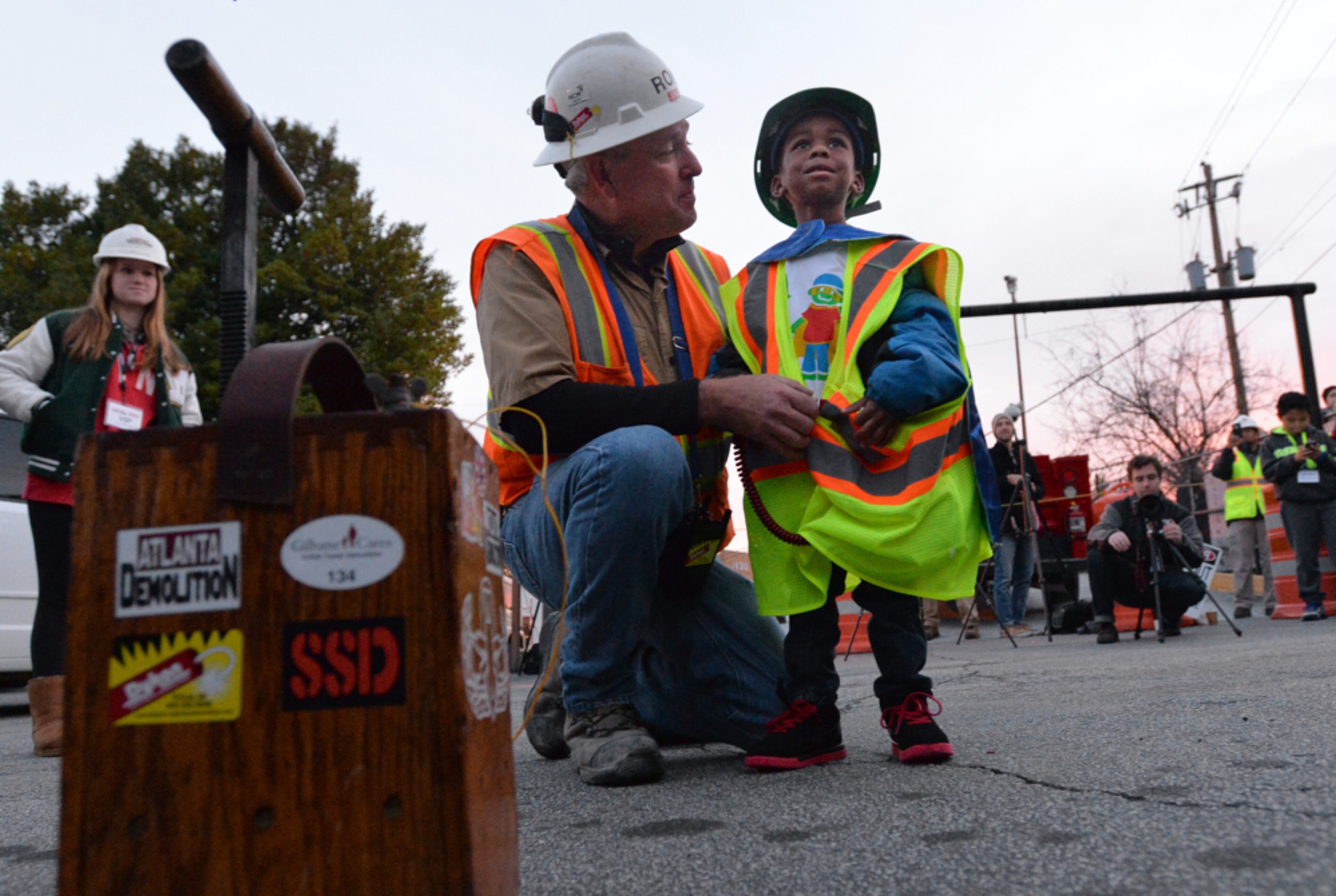 DJ ON THE JOB--November 8, 2014 Atlanta - 4-year-old "Super DJ," DJ Pitts, gets instructions from Ron Gilbert, project Manager at Dykon Explosive Demolition, before DJ pushes the button to implode the 19-story former Executive Park Motor building at the corner of I-85 and North Druid Hills Road on Saturday morning, November 8, 2014. One superhero patient at Children's Healthcare of Atlanta, four-year-old DJ Pitts, wore many capes during his six-month hospital stay after accidentally swallowing a dangerous engine cleaning material. From Batman and Superman capes to a homemade cape that proudly said "Super DJ," he has overcome near impossible obstacles. When he dons a cape, nothing is out of reach. To show support for DJ and brave kids like him, the Atlanta community was celebrating Cape Day ATL to surprise and delight Children's patients with photos on social media that show residents wearing capes in their honor. The morning after Cape Day, on Saturday, Nov. 8, DJ and a group of superheroes demonstrated their strength and bravery by pressing a button that imploded a 19-story building. The property is the former Executive Park Motor building at the corner of I-85 and North Druid Hills Road. HYOSUB SHIN / HSHIN@AJC.COM