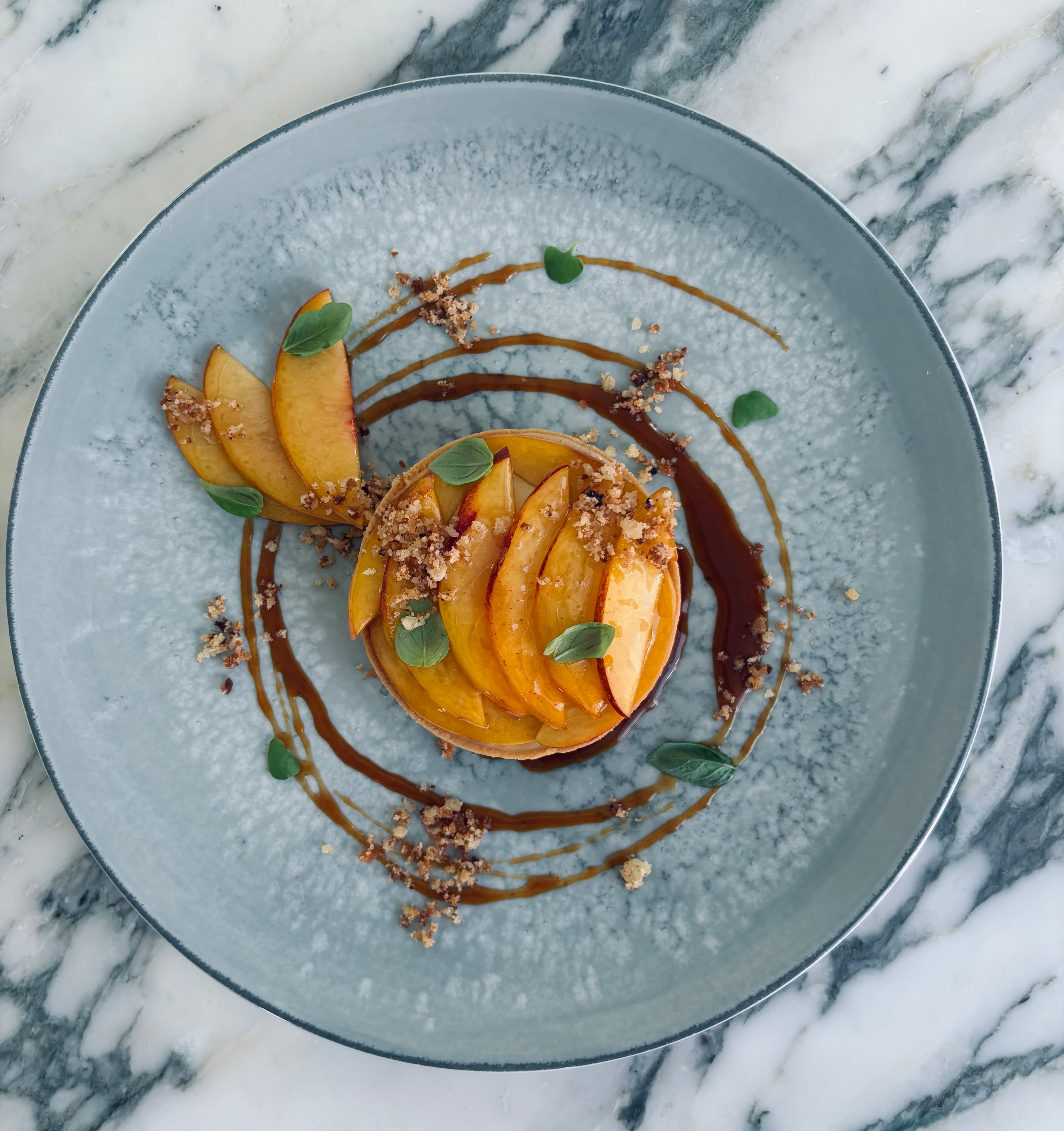The peach tart at Elise: peach-vanilla custard topped with peach slivers, ginger crumble and micro-basil, with salted caramel swirls. (Courtesy of Elise)